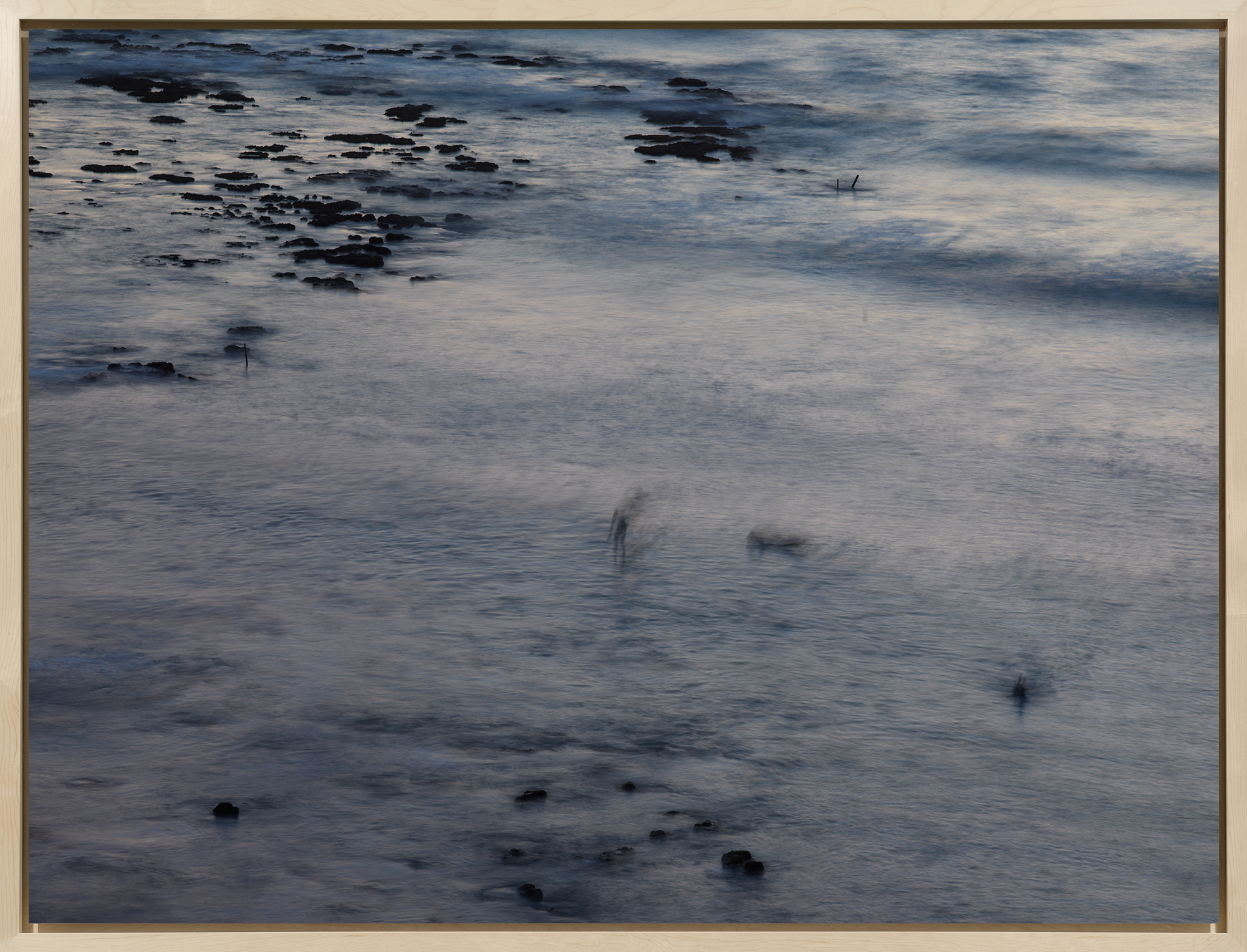 Color photograph of surfer on water with rocks and motion blur framed in bleached wood