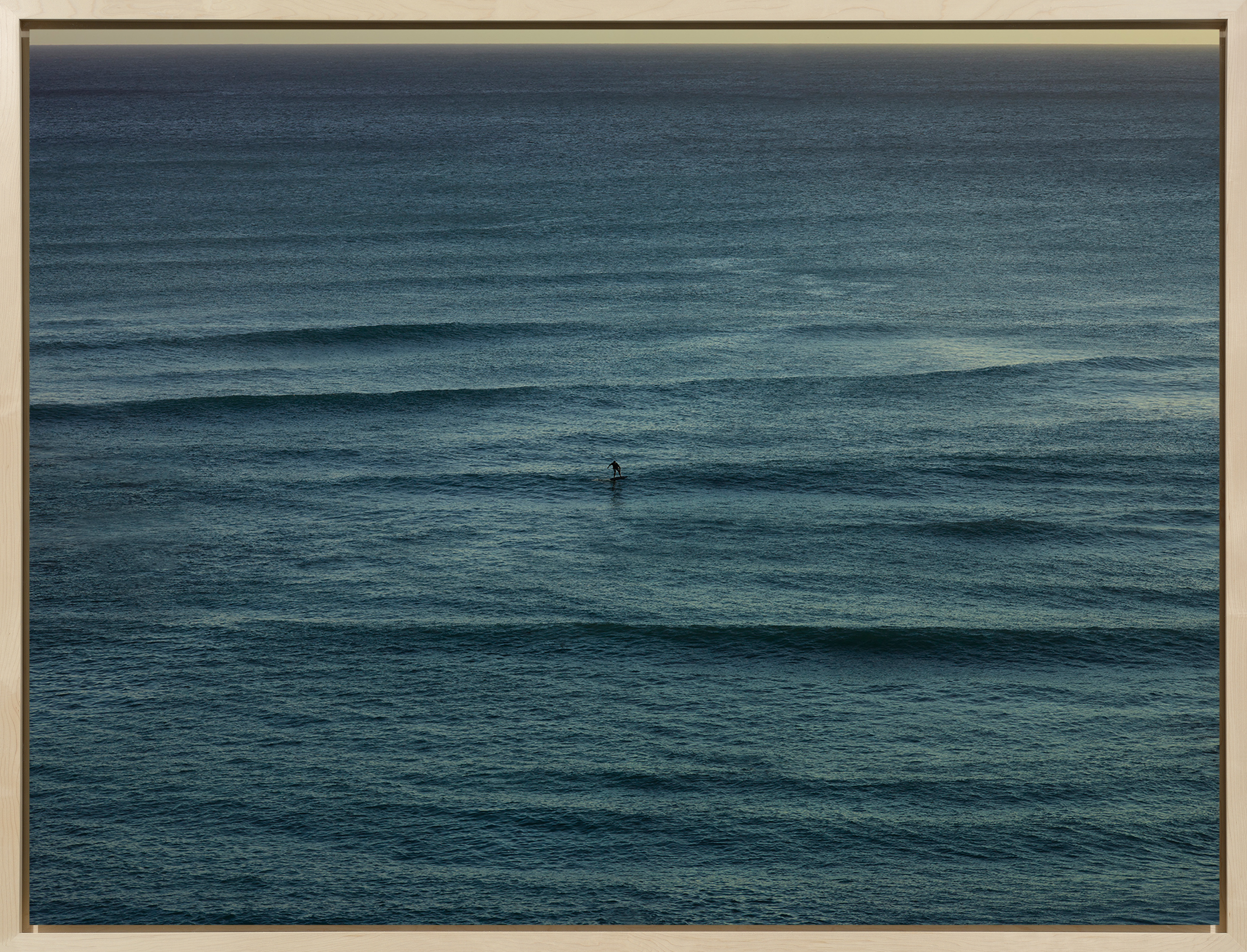 Color photograph of a surfer riding waves on the middle of the ocean framed in bleached wood