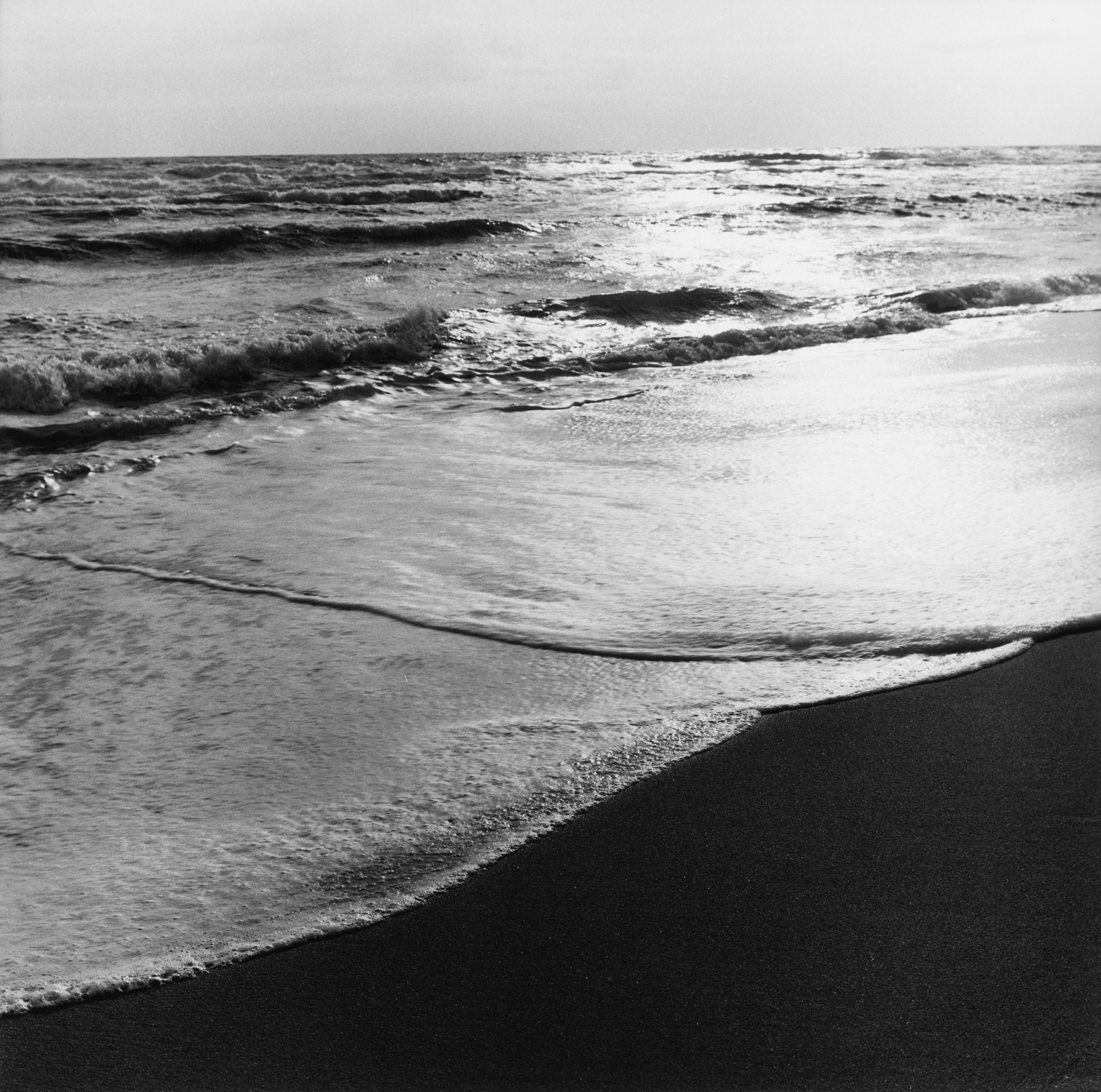 Black and white photograph of ocean waves crashing onto the beach