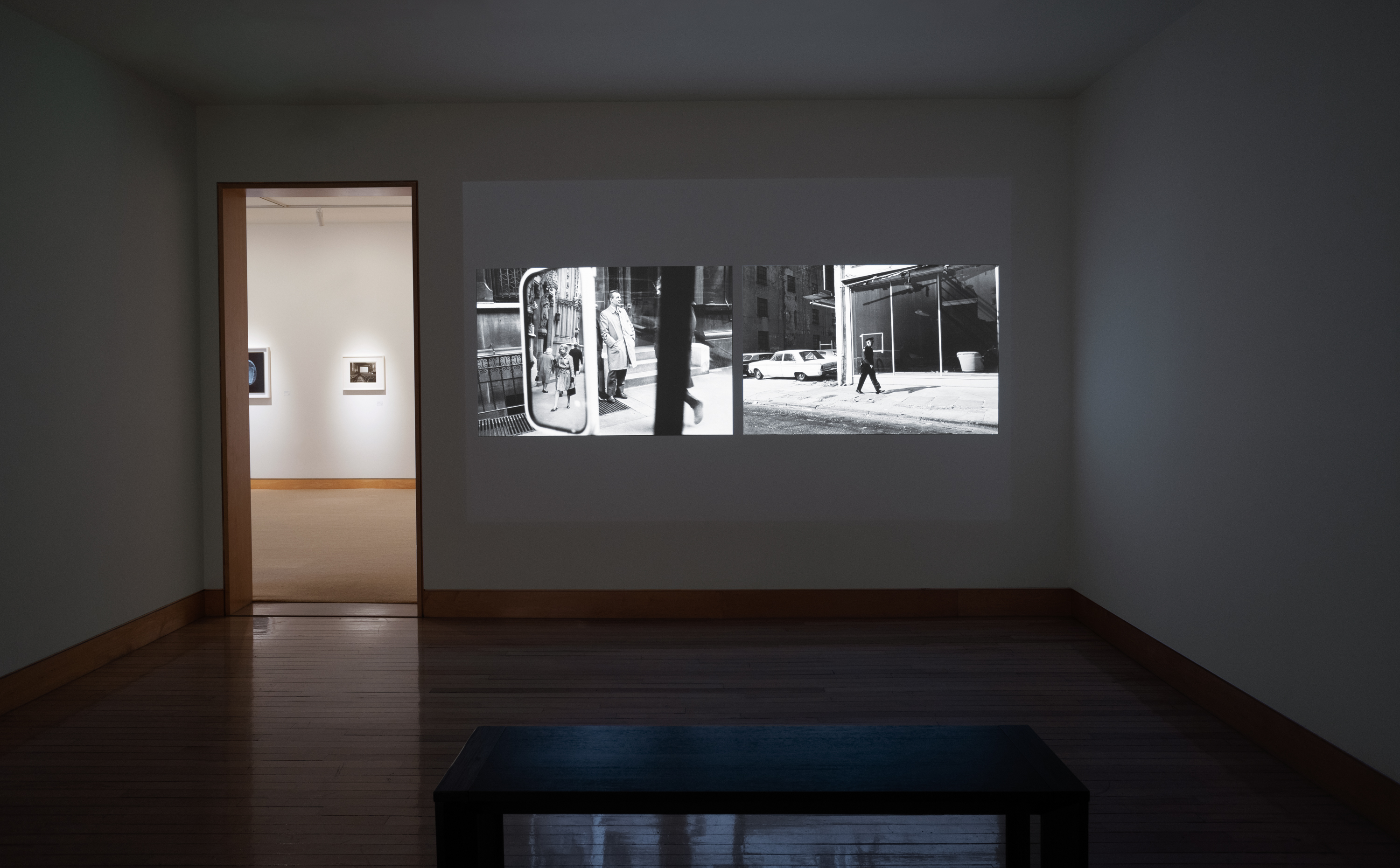 Color image of a gallery exhibiting black and white photographs via projection onto white gallery wall