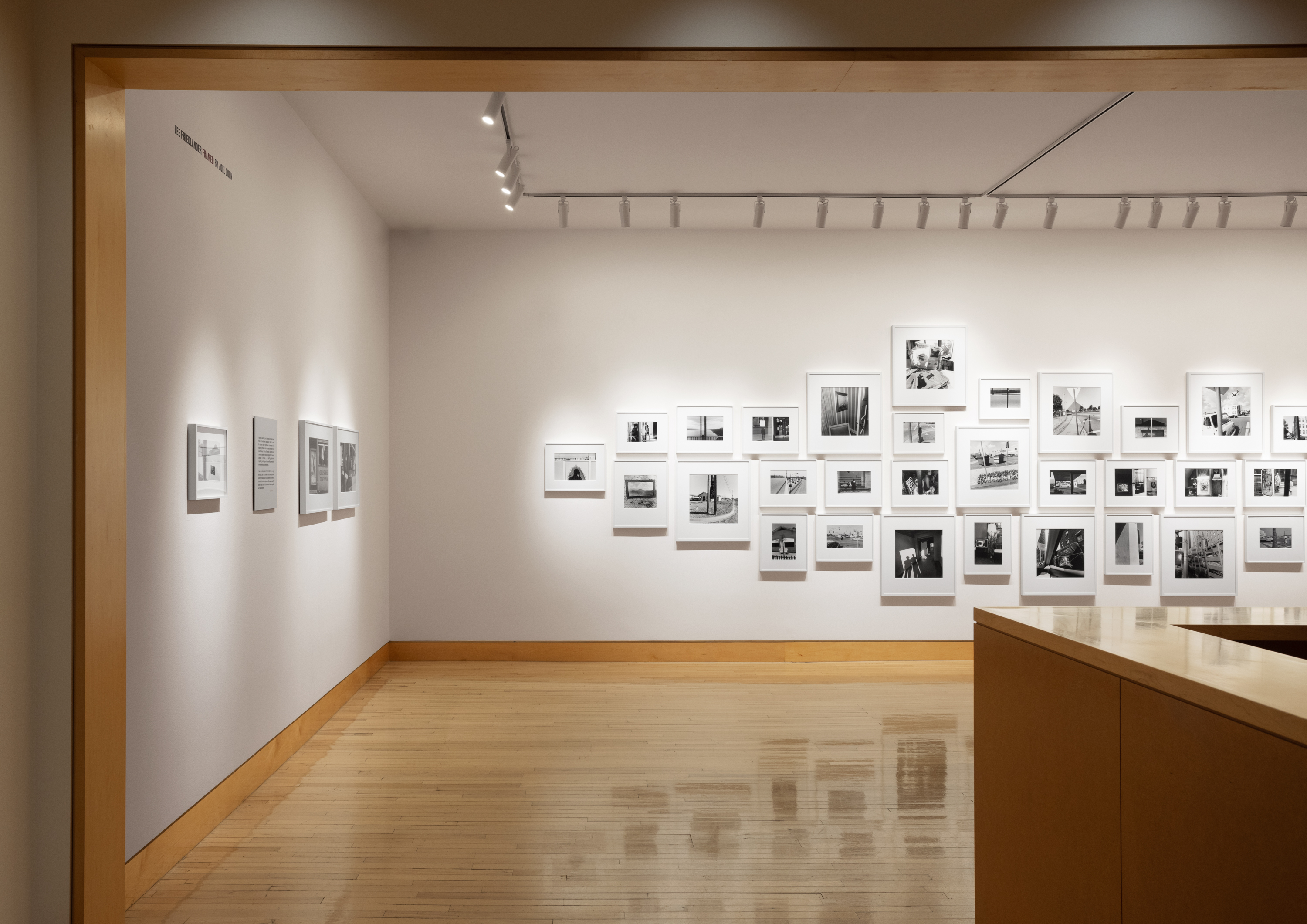 Color image of a gallery entryway exhibiting black and white photographs of various sizes on white gallery walls