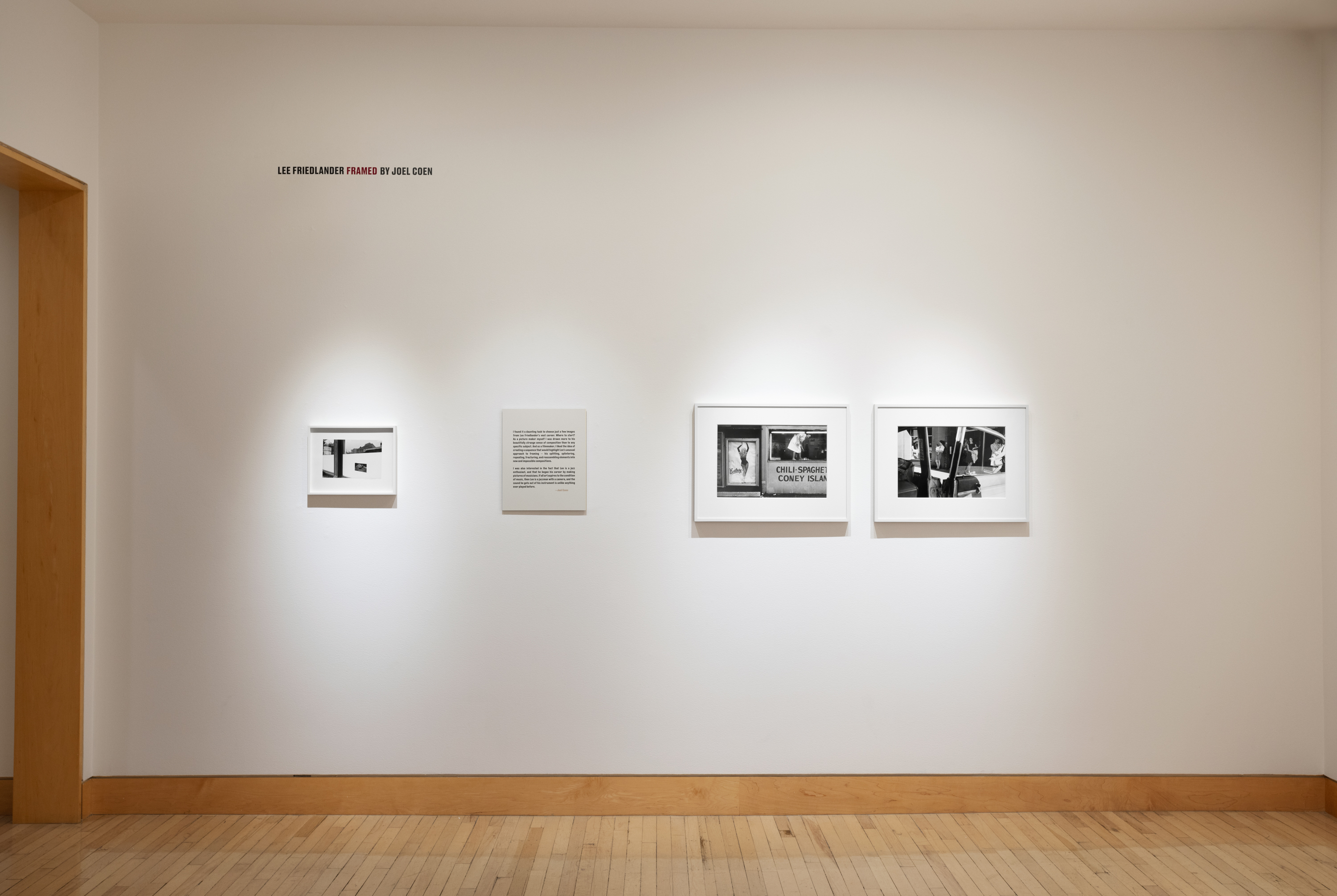 Color image of a gallery exhibiting black and white photographs of various sizes on white gallery wall with exhibition text
