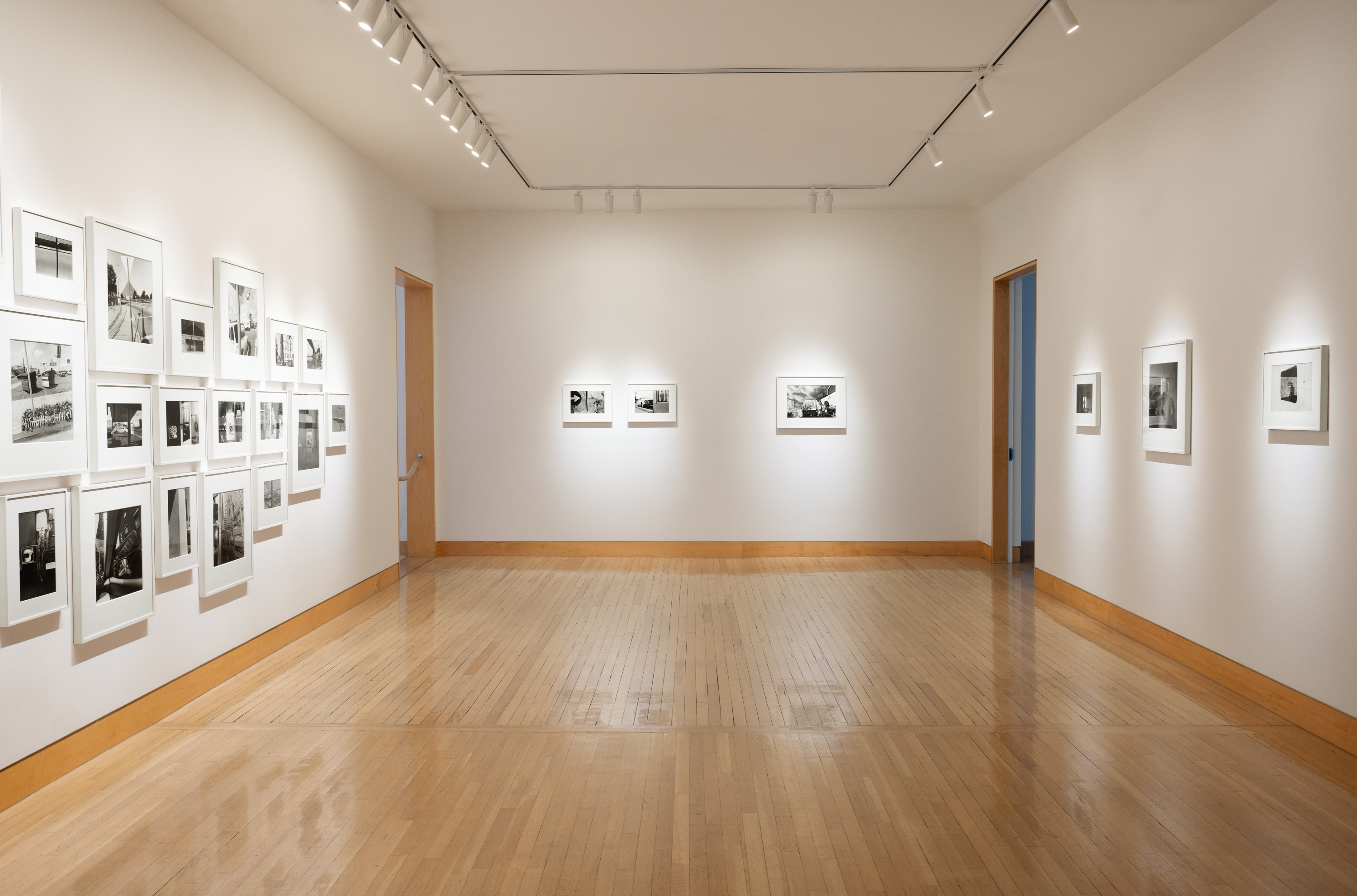 Color image of a gallery exhibiting black and white photographs of various sizes on white gallery walls