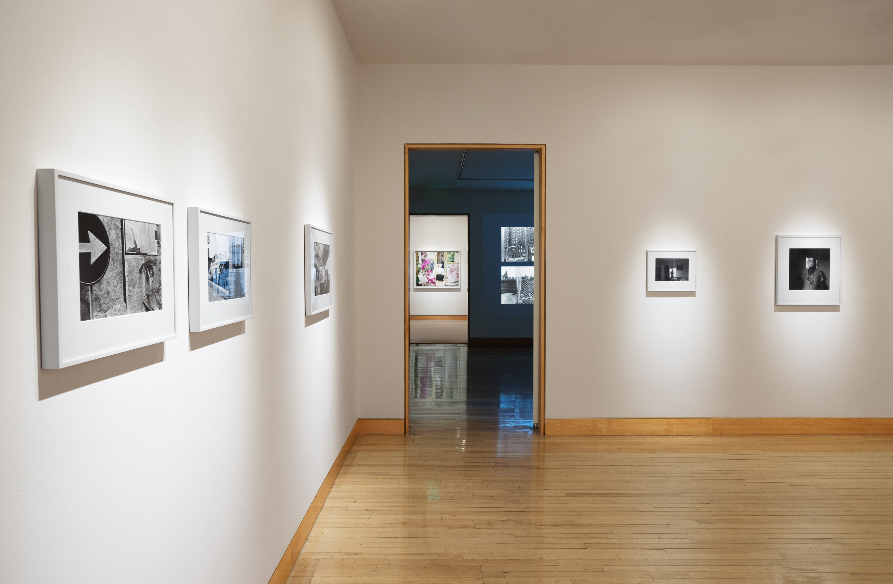 Color image of a gallery exhibiting black and white photographs of various sizes on white gallery walls
