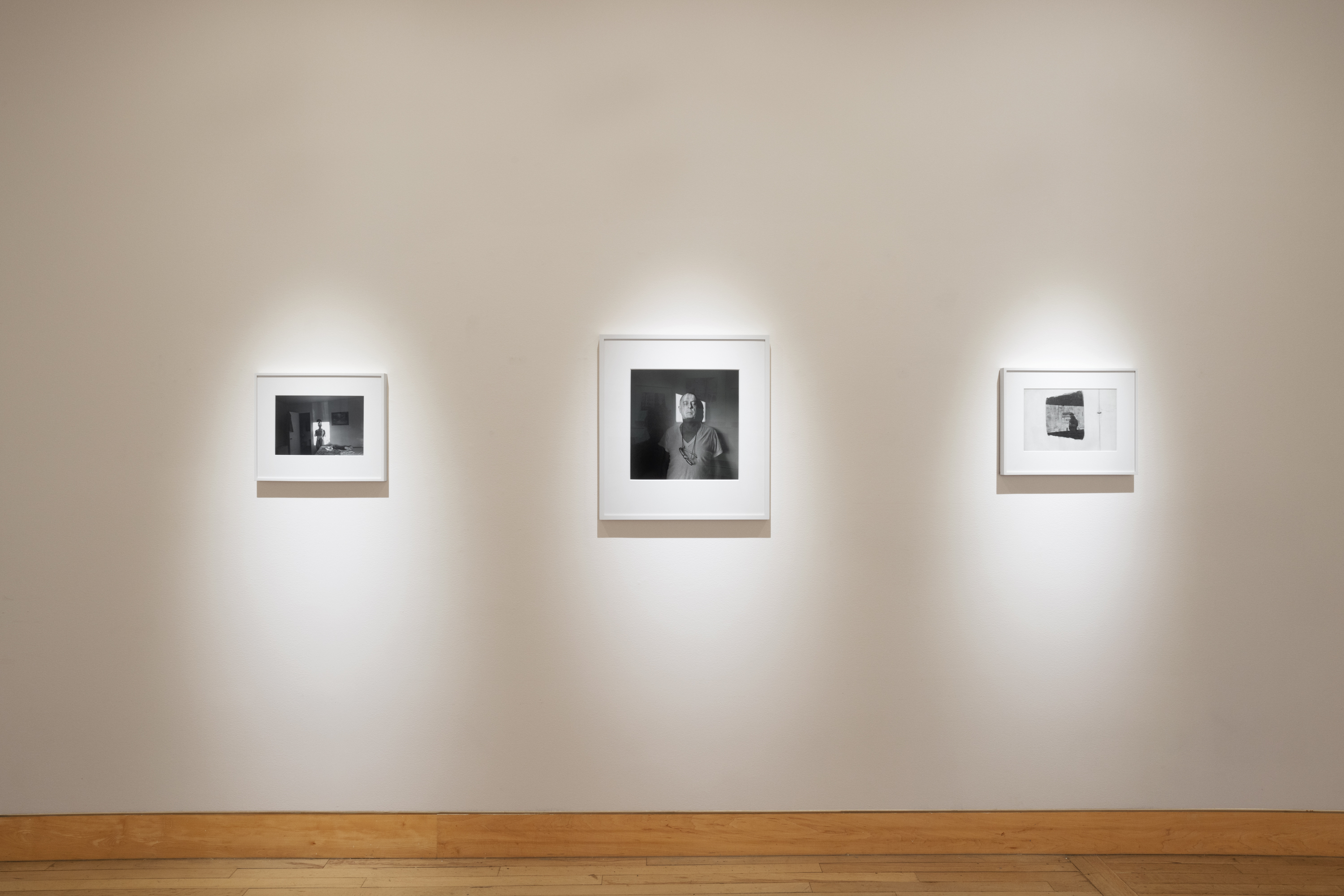 Color image of a gallery exhibiting black and white photographs of various sizes on white gallery wall