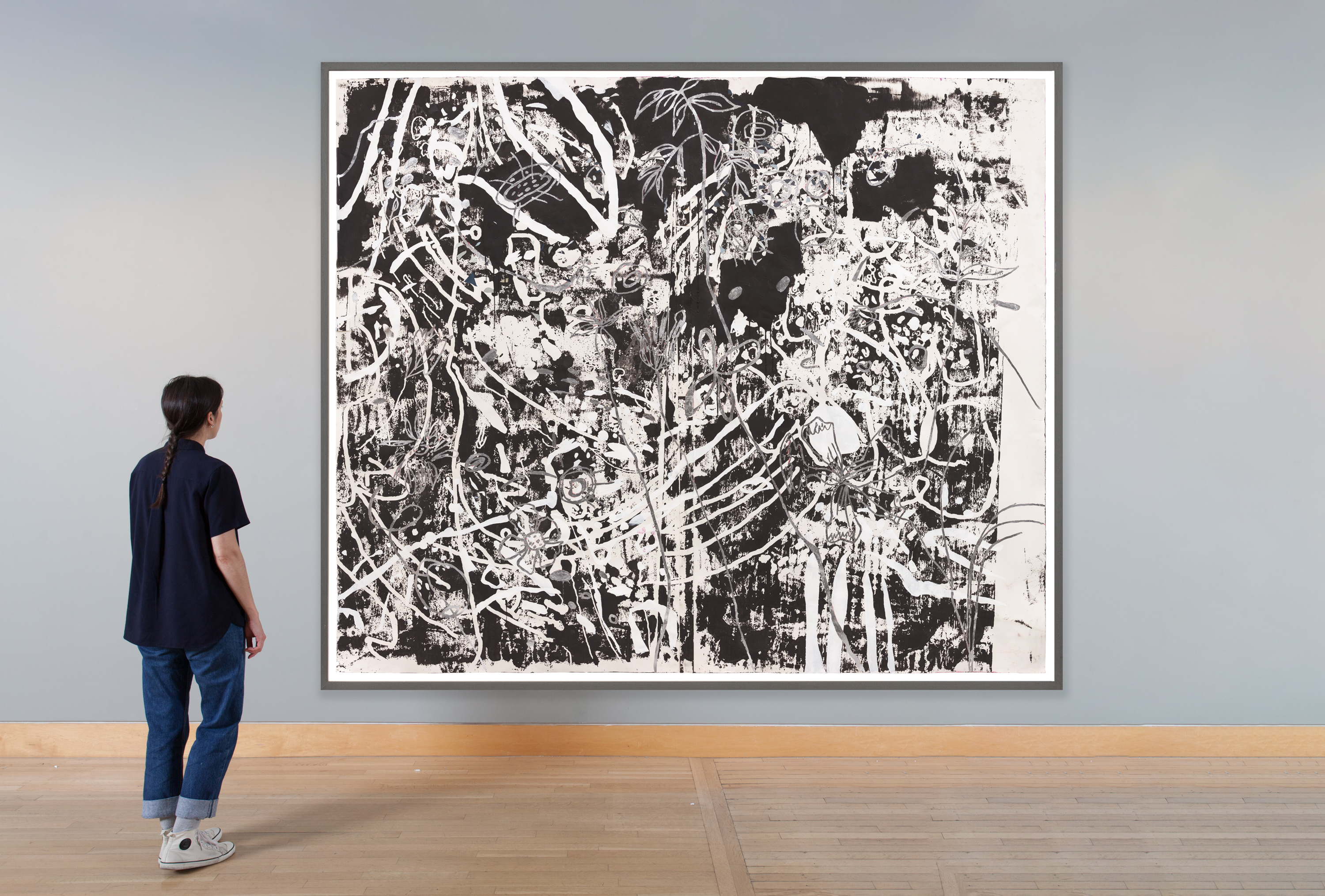 Color image of a black and white mixed media artwork with flowers and abstract forms framed in grey on grey gallery wall