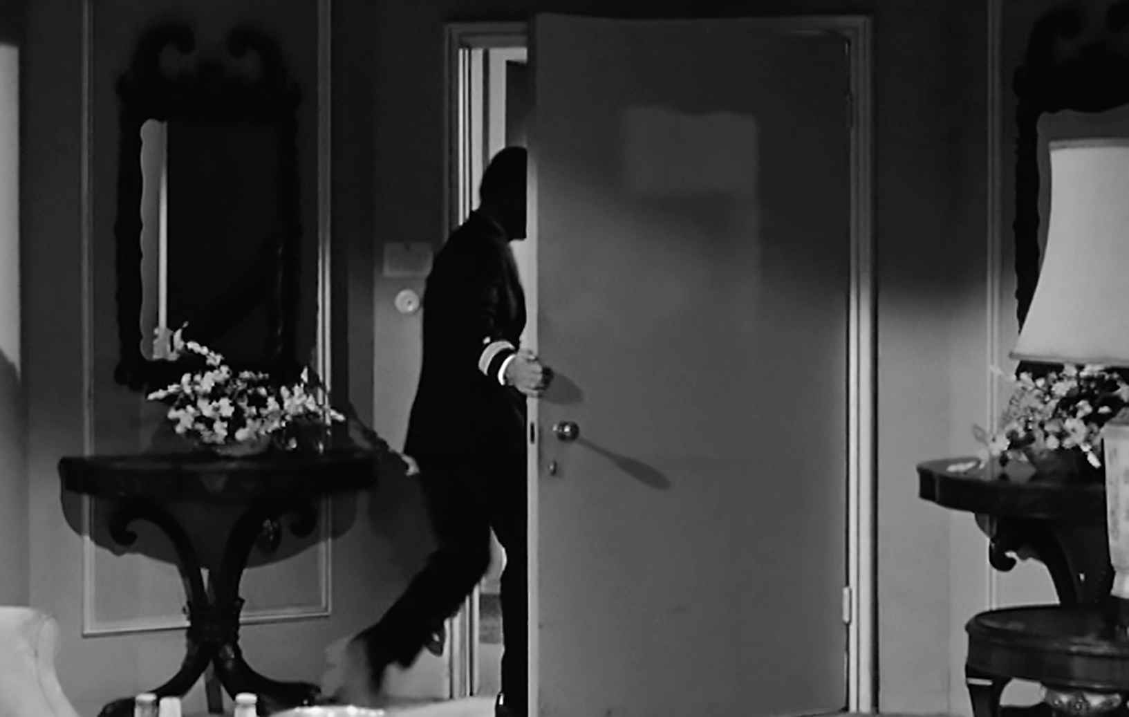 Black and white still of a figure exiting a room