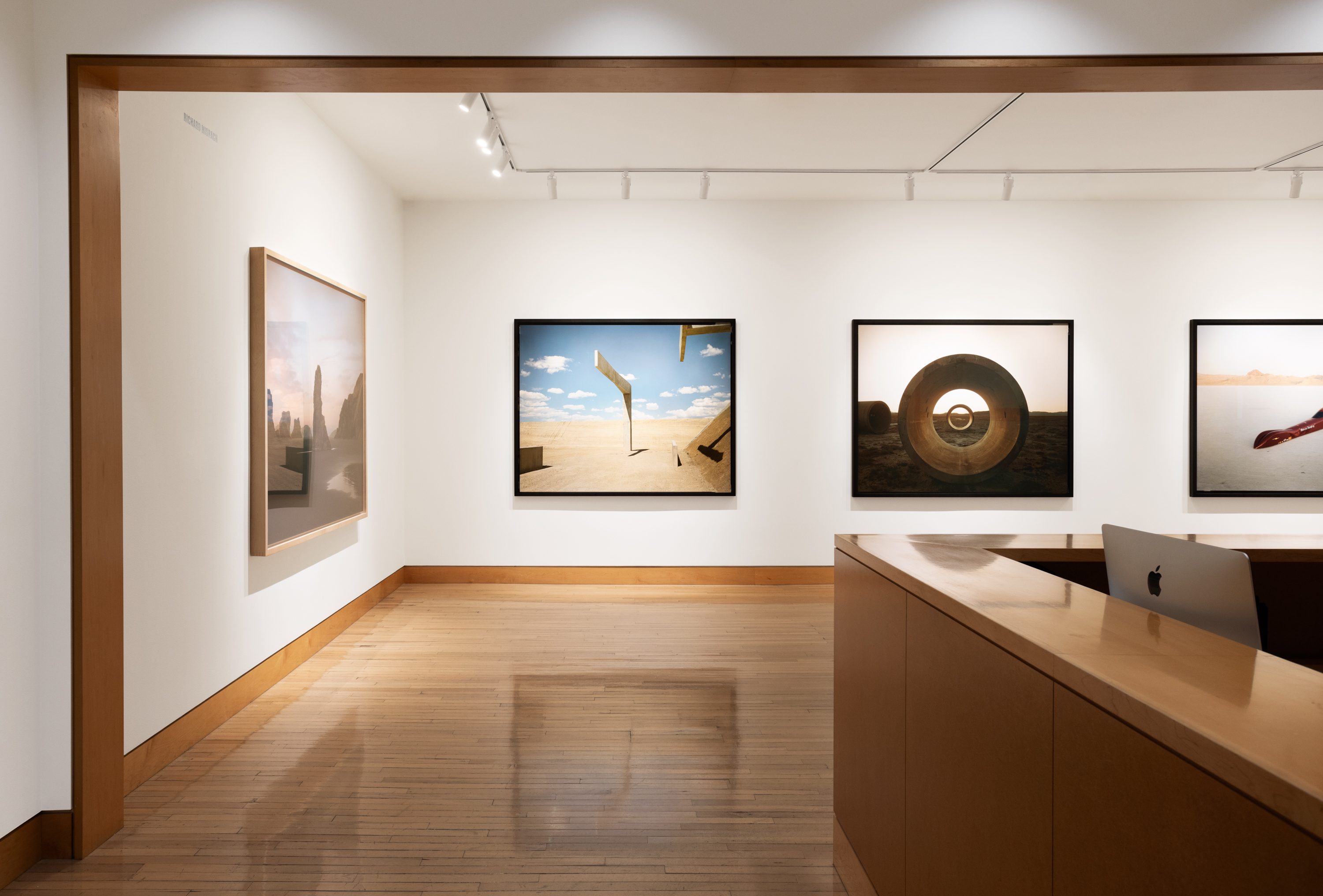 Color image of a gallery entryway exhibiting color photographs of various landscapes on white walls