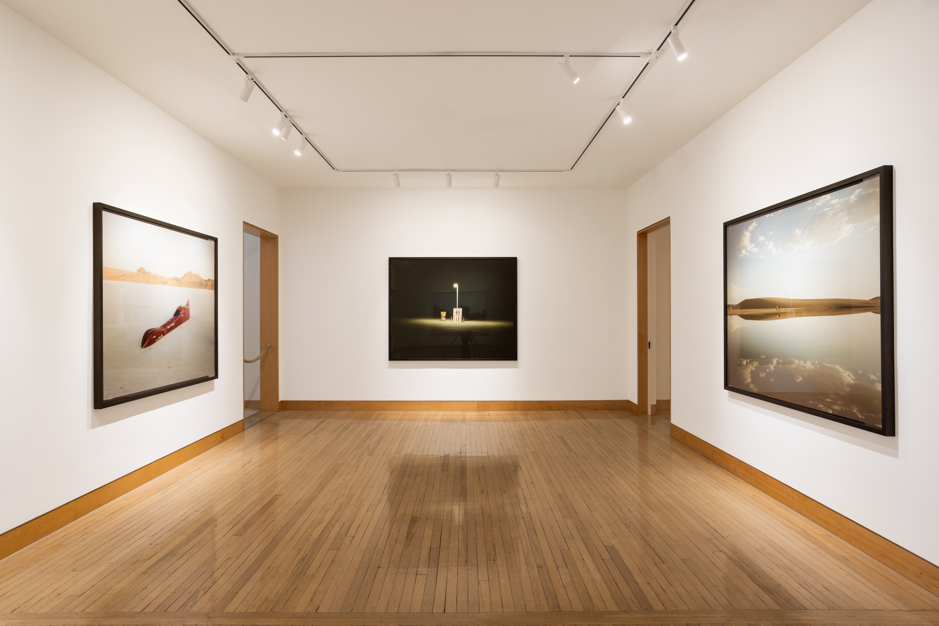 Color image of three color photographs depicting various desert scenes framed in black on white gallery walls