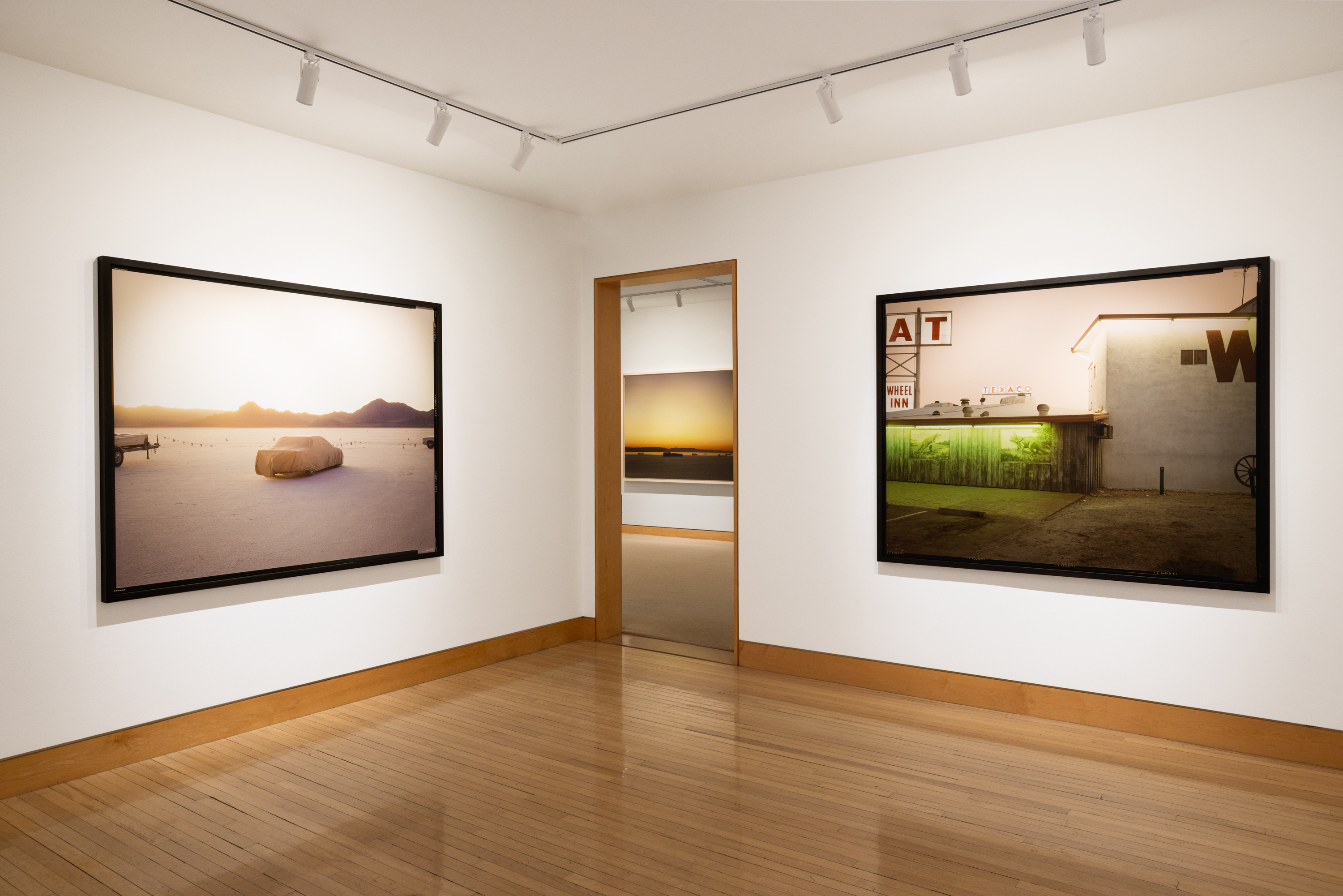 Color image of three color photographs framed in bleached wood and black on white gallery walls