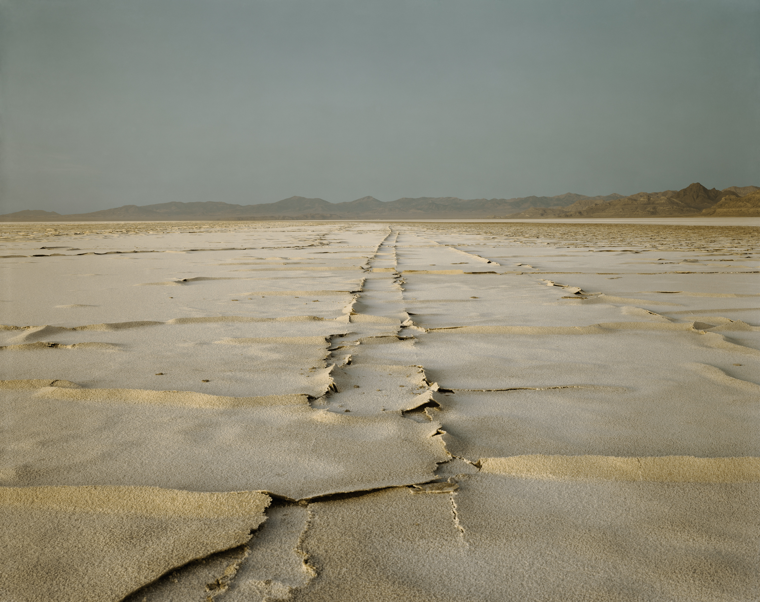 Color photograph of encrusted tracks on salt flats with mountain range on the horizon