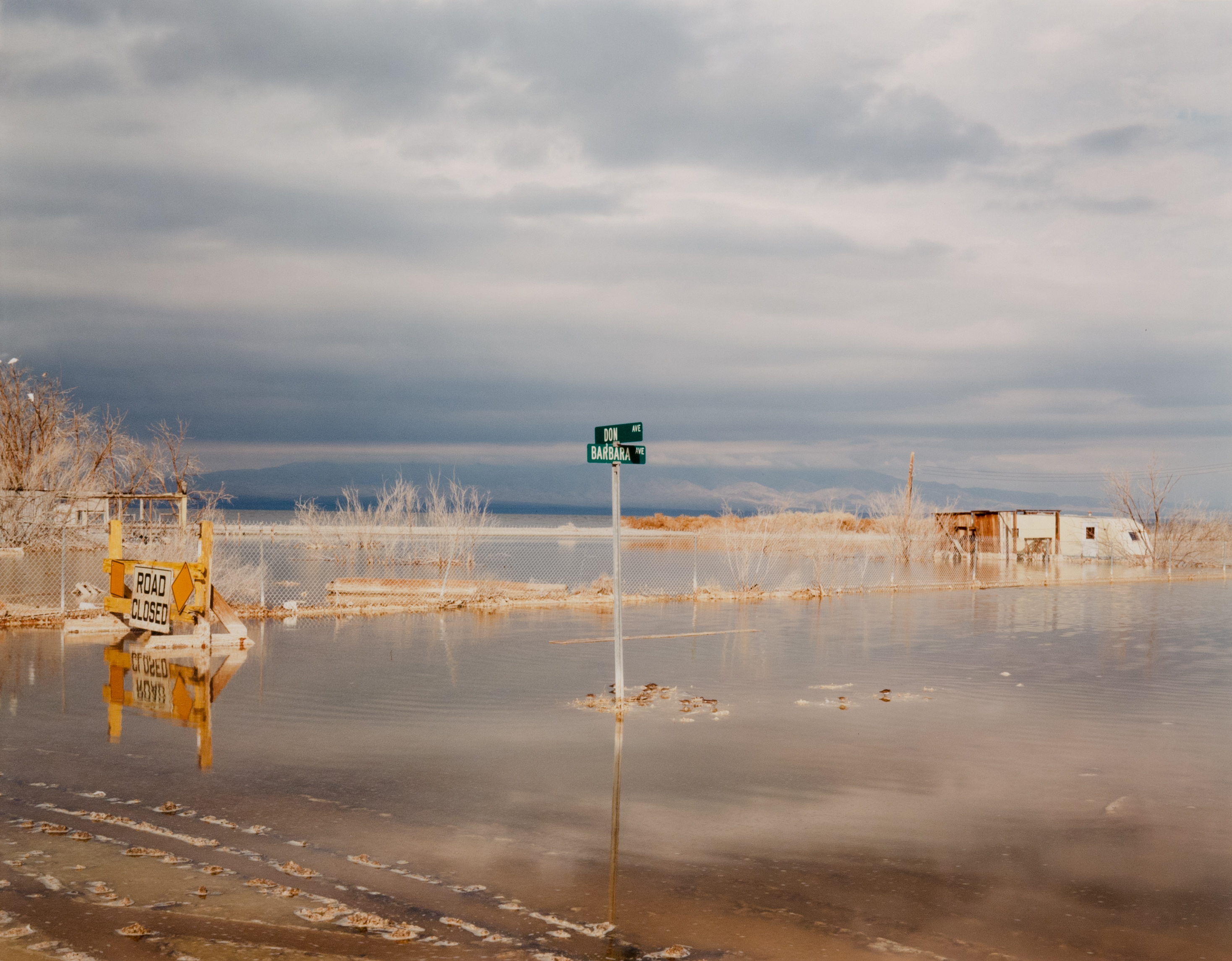 Color photograph of a submerged street with a street sign in the center and mountain range on the horizon