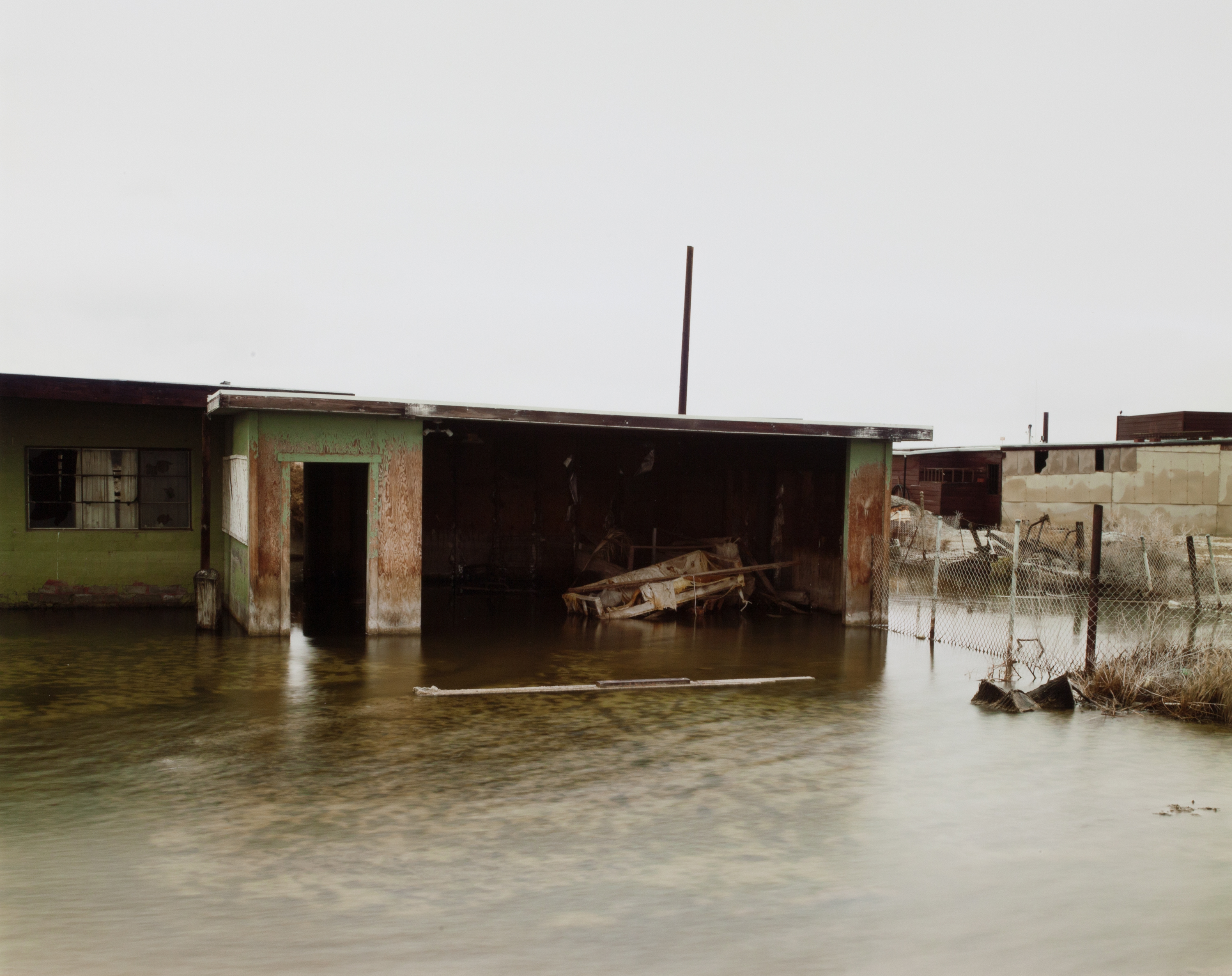 Color photograph of a flooded abandoned garage with a distressed rowboat
