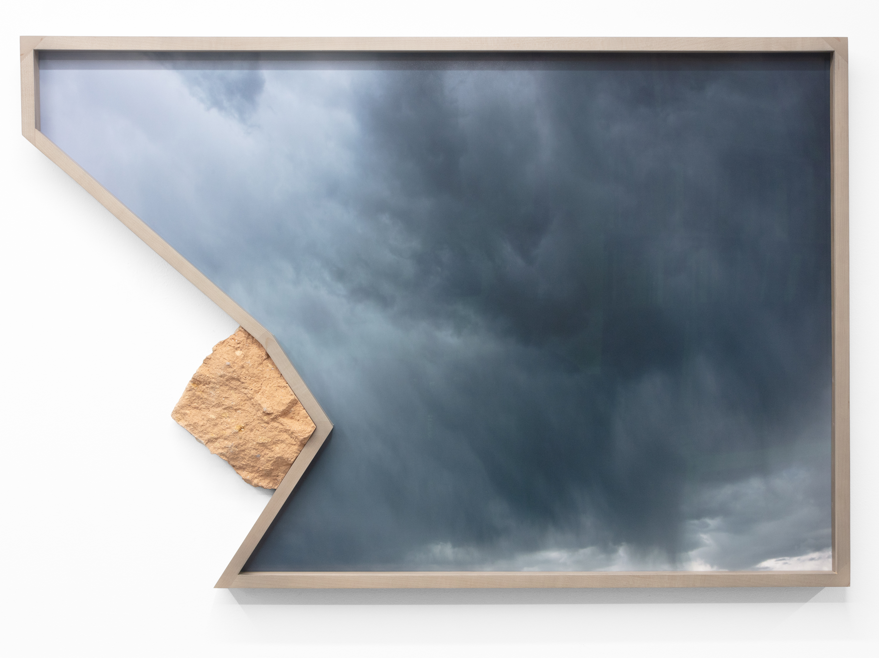 Color image of a color photograph of a grey sky framed in natural wood with a modified rock on the frame