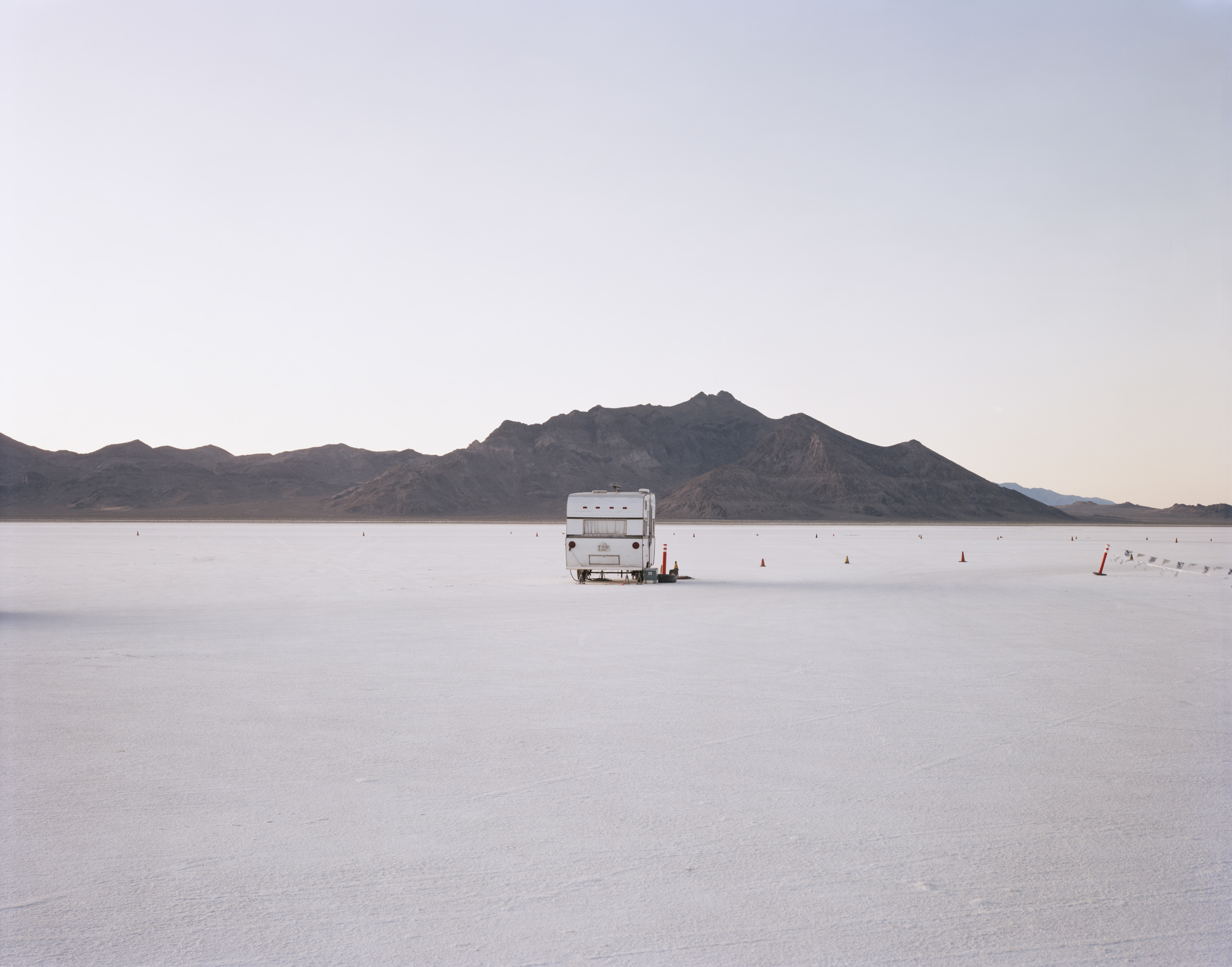 Color photograph of a camper in the middle of salt flats with mountains along the horizon