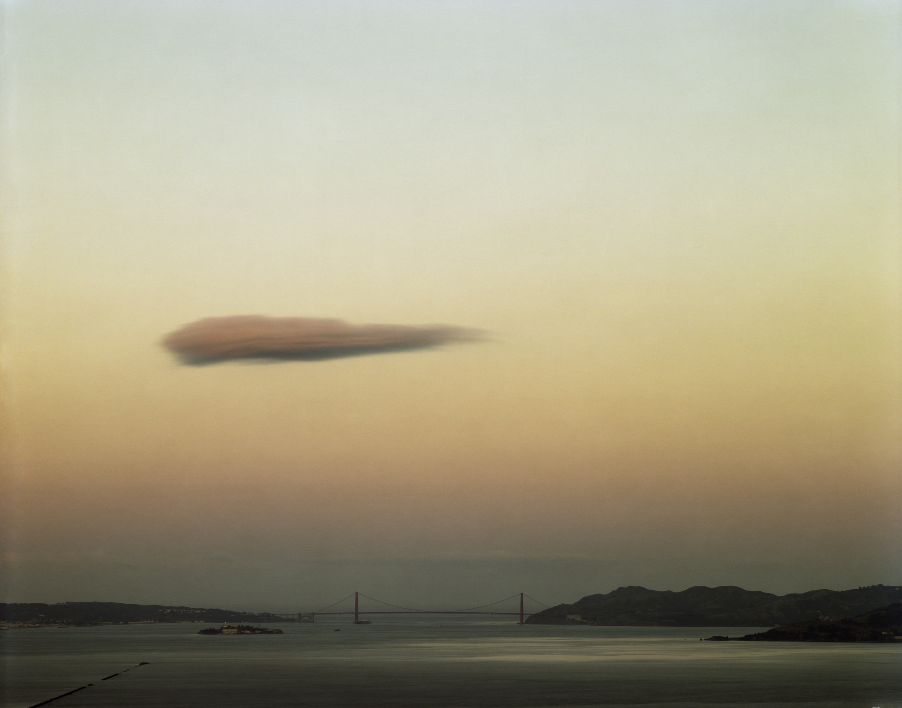 Color photograph of San Francisco Bay and Golden Gate Bridge during sunrise with a single cloud in the sky