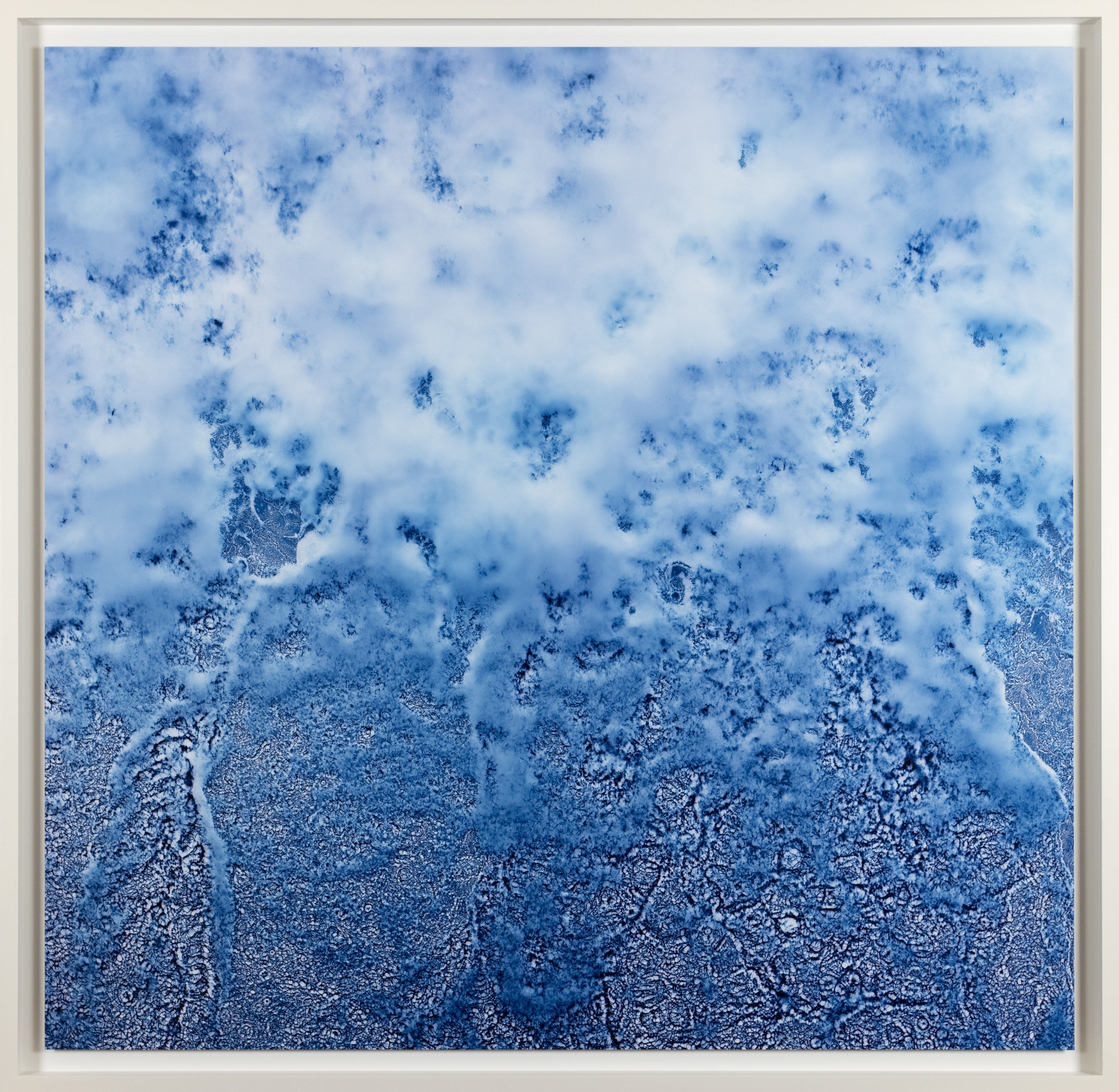 Color photograph of water crashing in blue hue framed in white