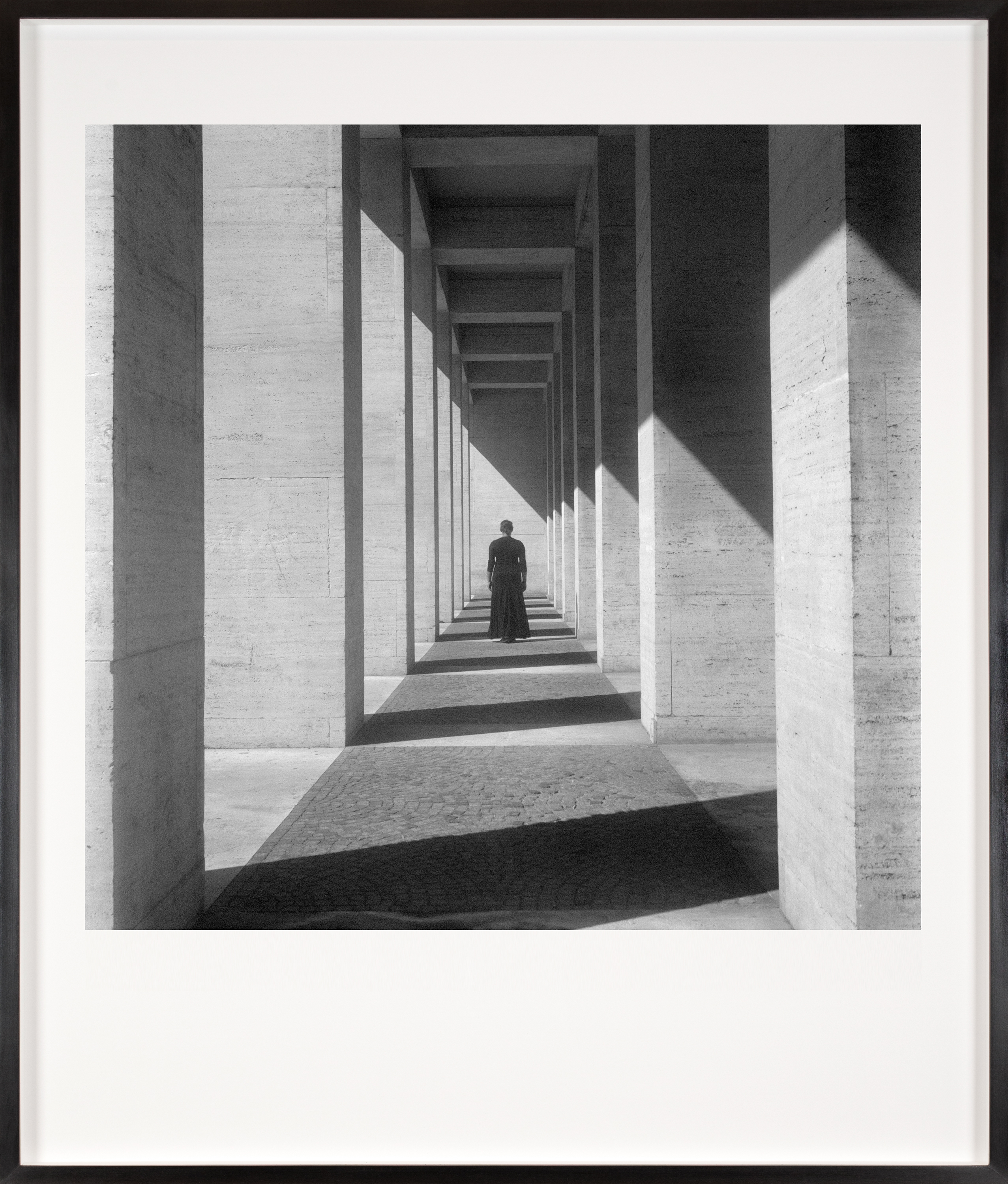 Black and white photograph of a figure in all black looking at concrete wall