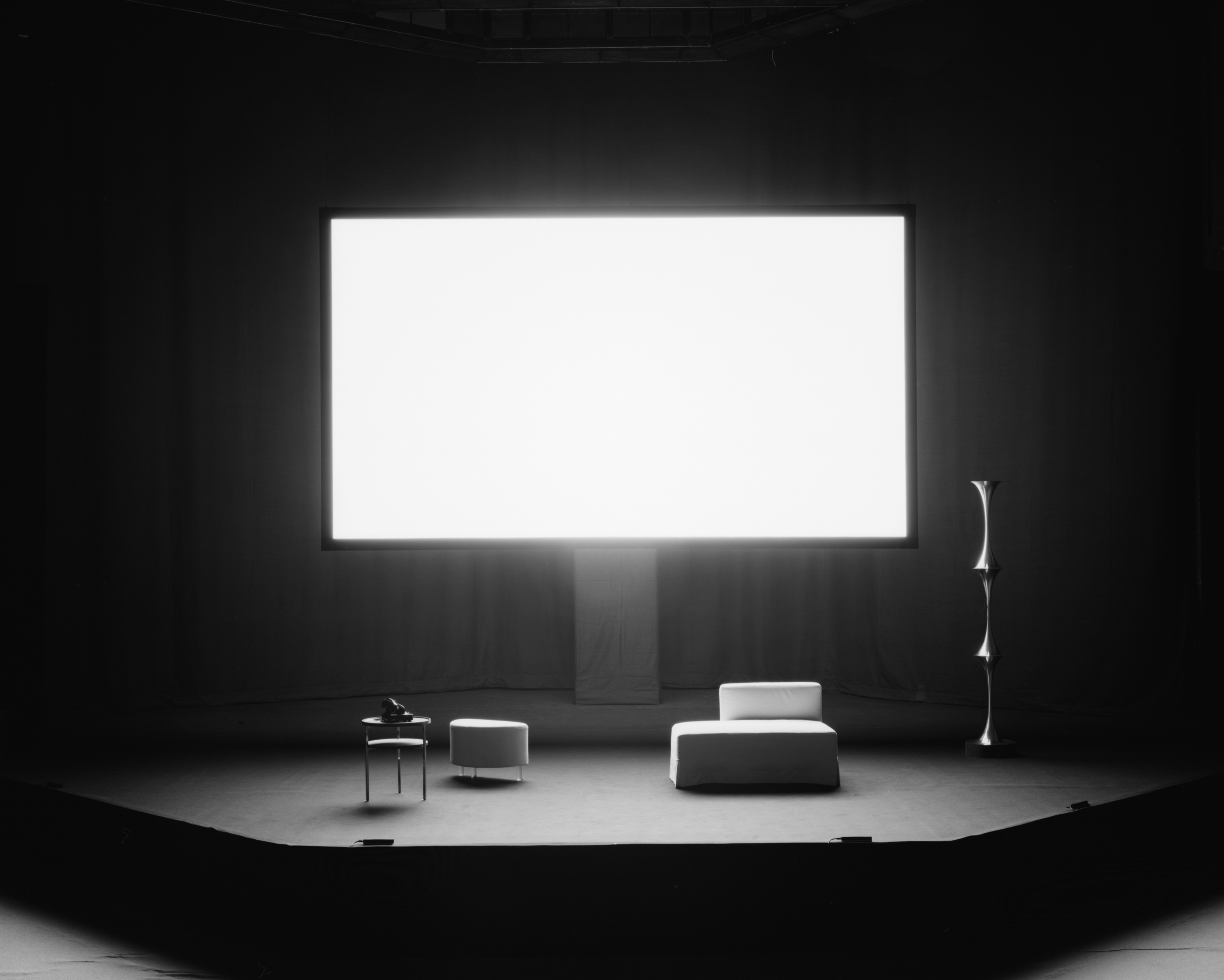 Black and white photograph of an empty stage with a blank white screen illuminating the space