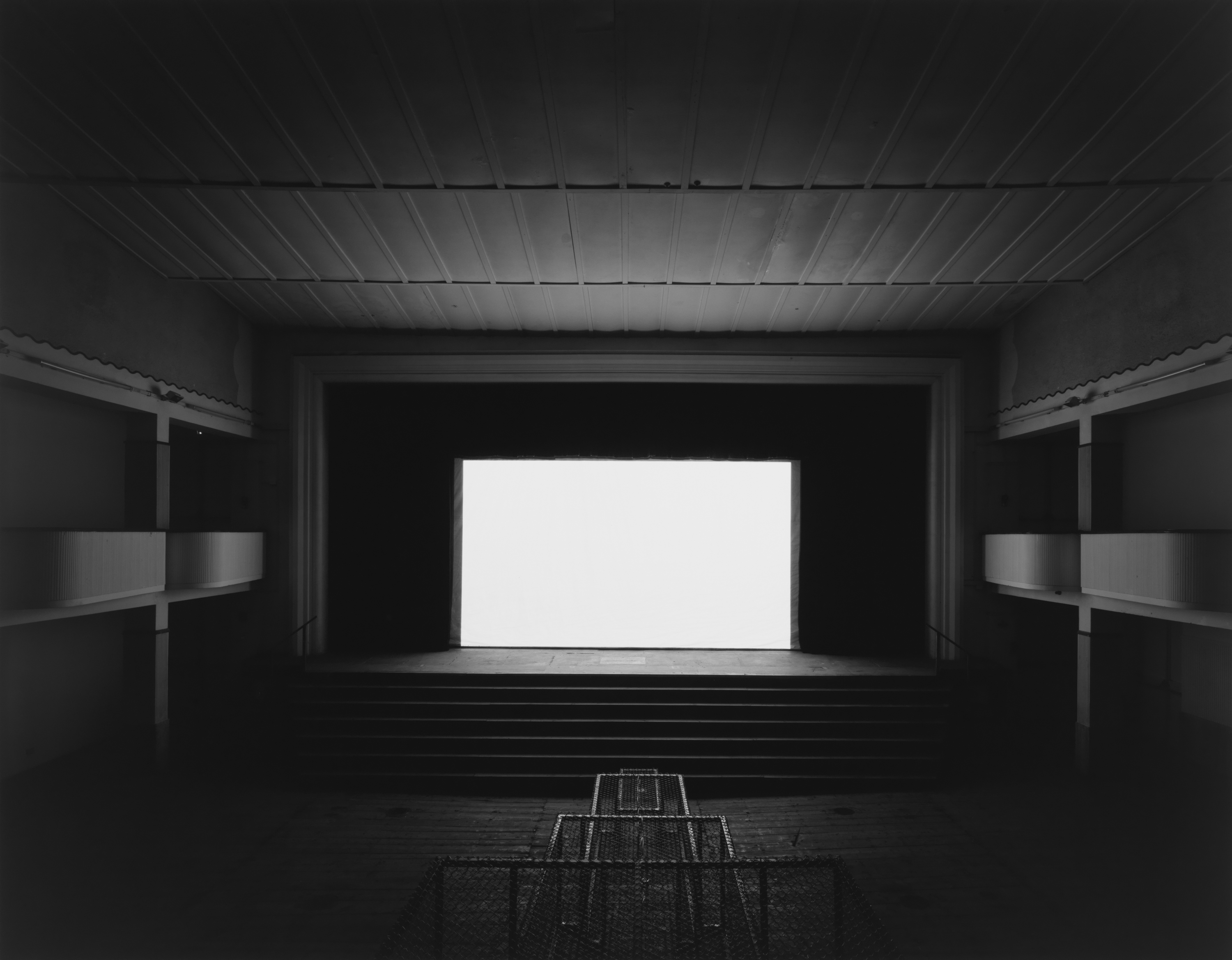 Black and white photograph of an empty theater with a blank white screen illuminating the space