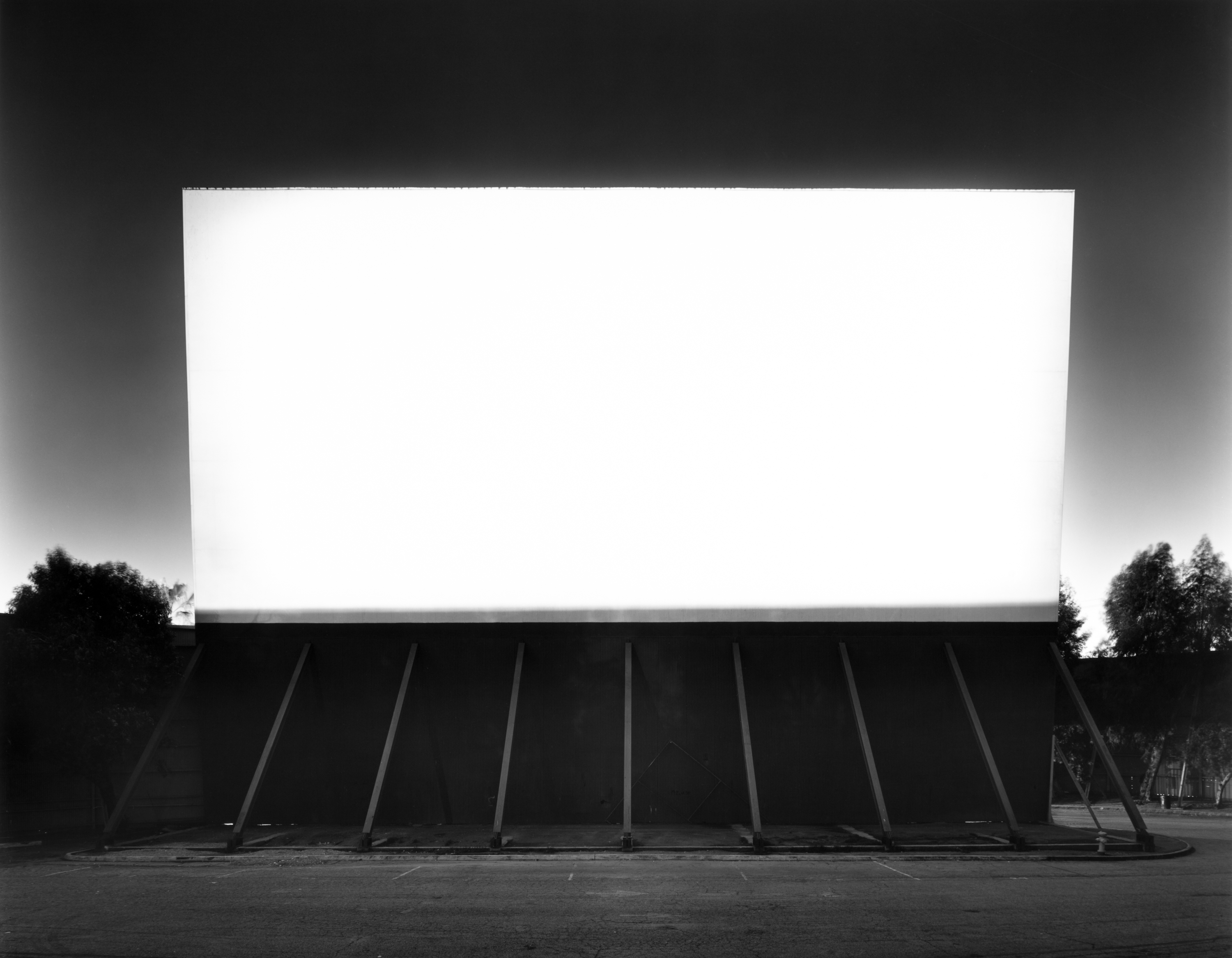 Black and white photograph of an empty drive-in with a blank white screen illuminating the space