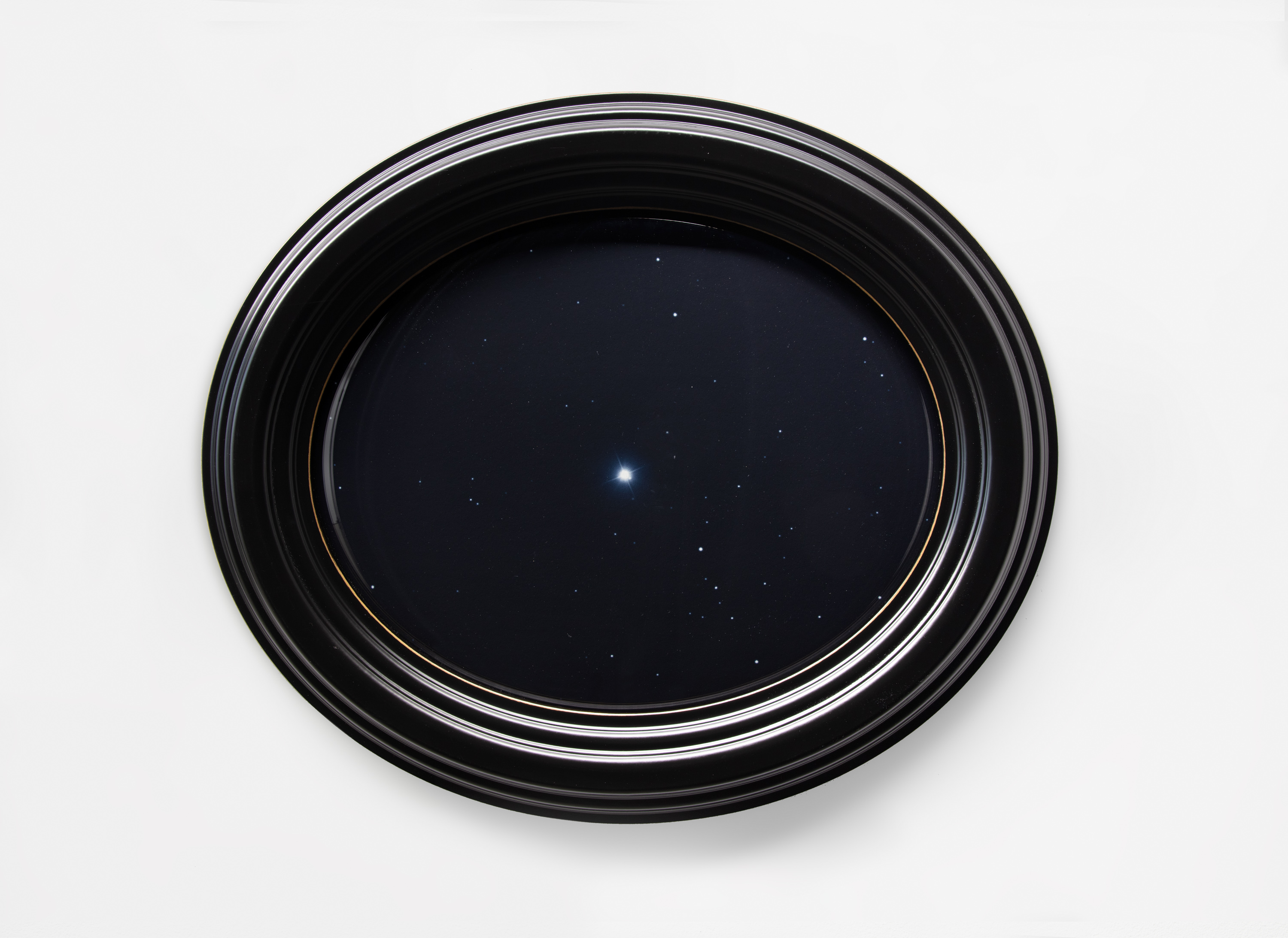 Image of an installed artwork of an oval framed photograph of the night sky, with the North Star in the center.