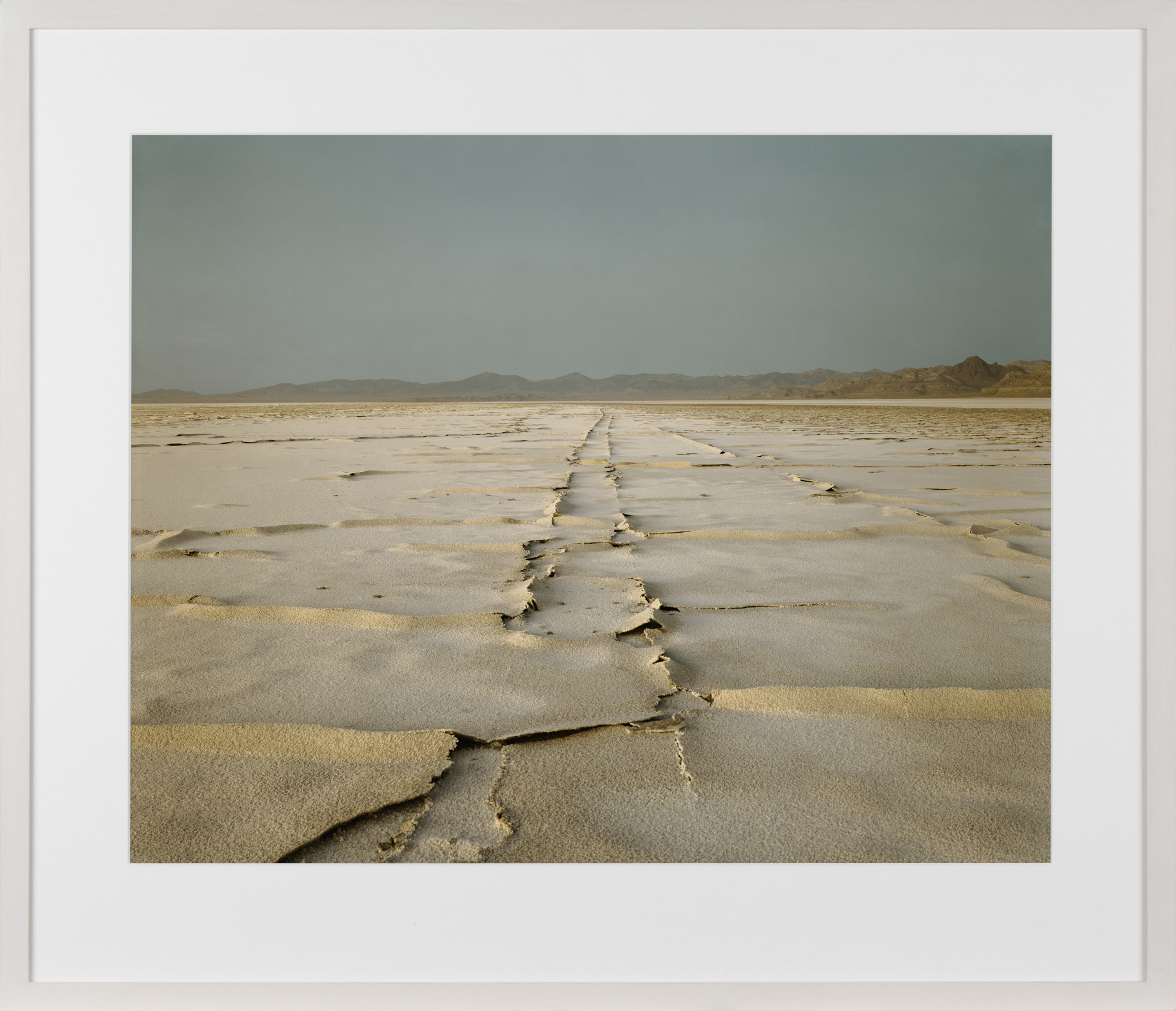 Color image of a color photograph depicting encrusted tracks in middle of desert framed in white