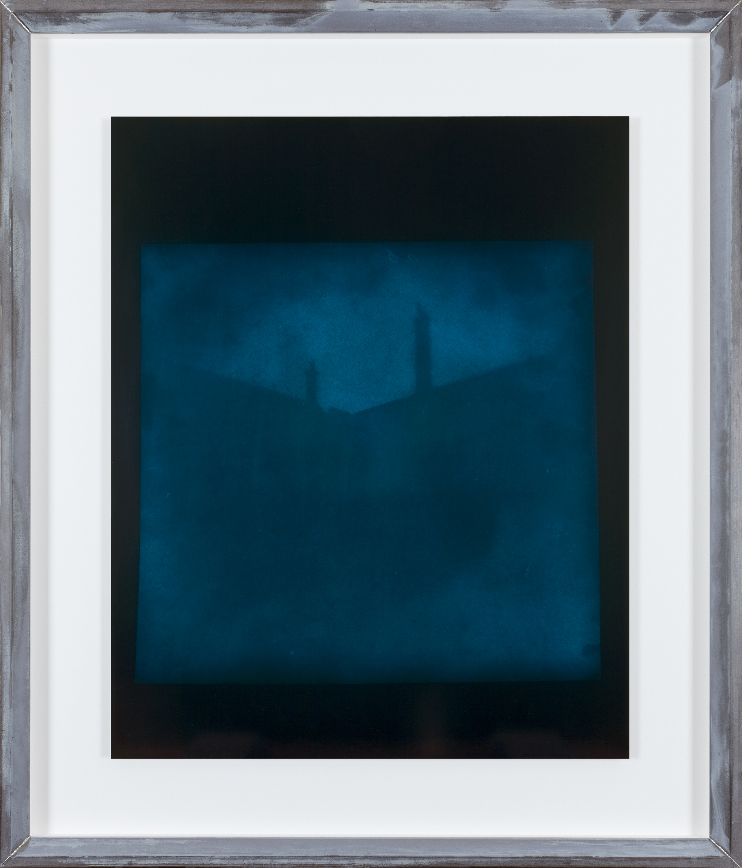 Color photograph of blue toned building by a black background in an aluminum frame