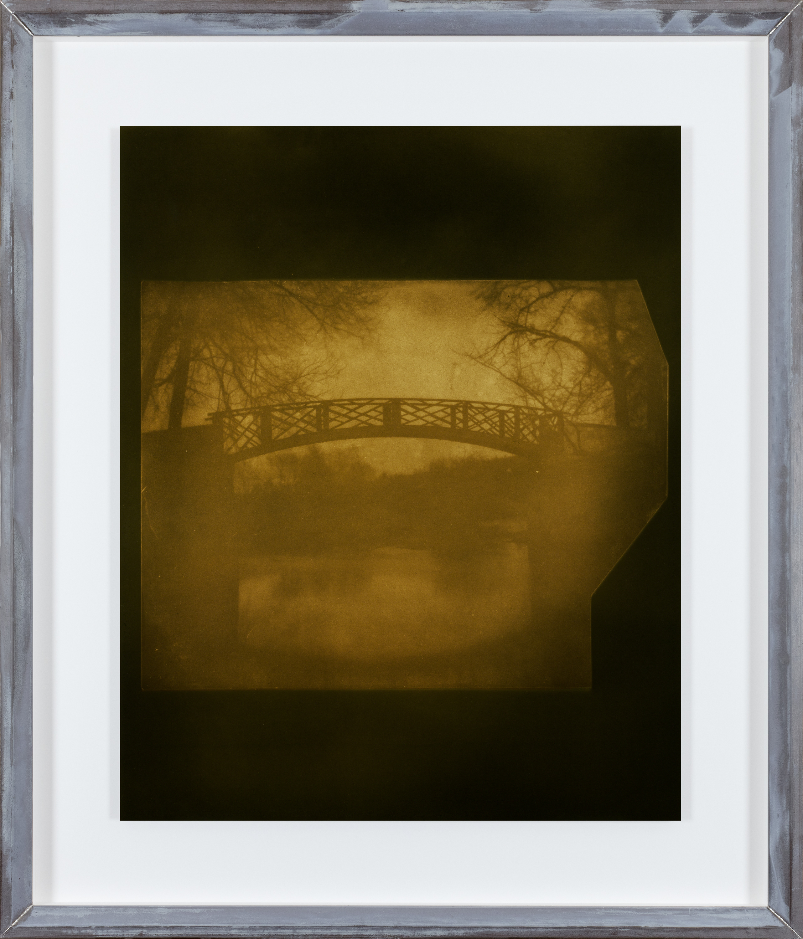Color photograph of a yellow toned bridge above a lake framed in an aluminum frame