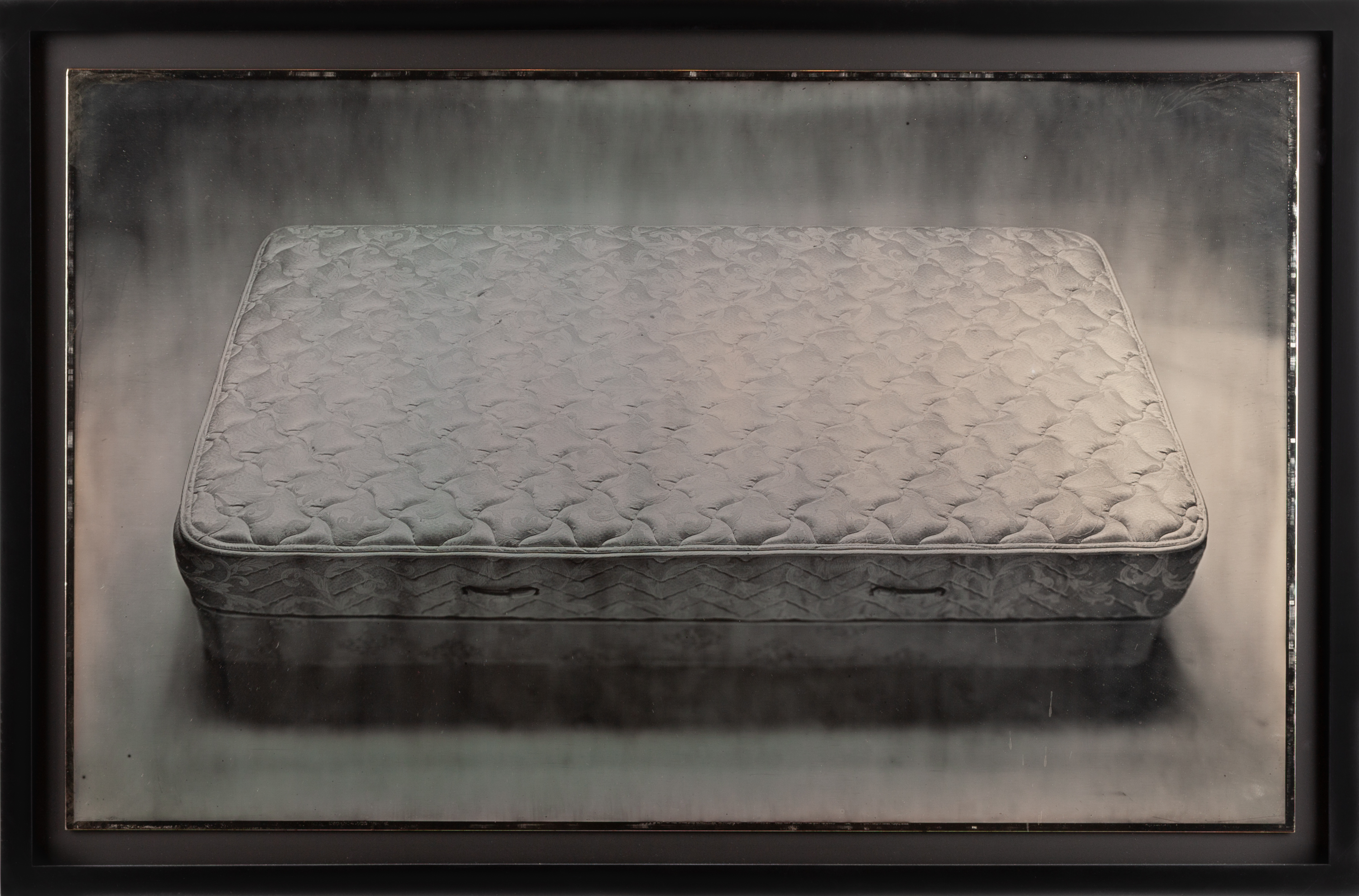 Color image of a daguerreotype depicting a a mattress framed in black