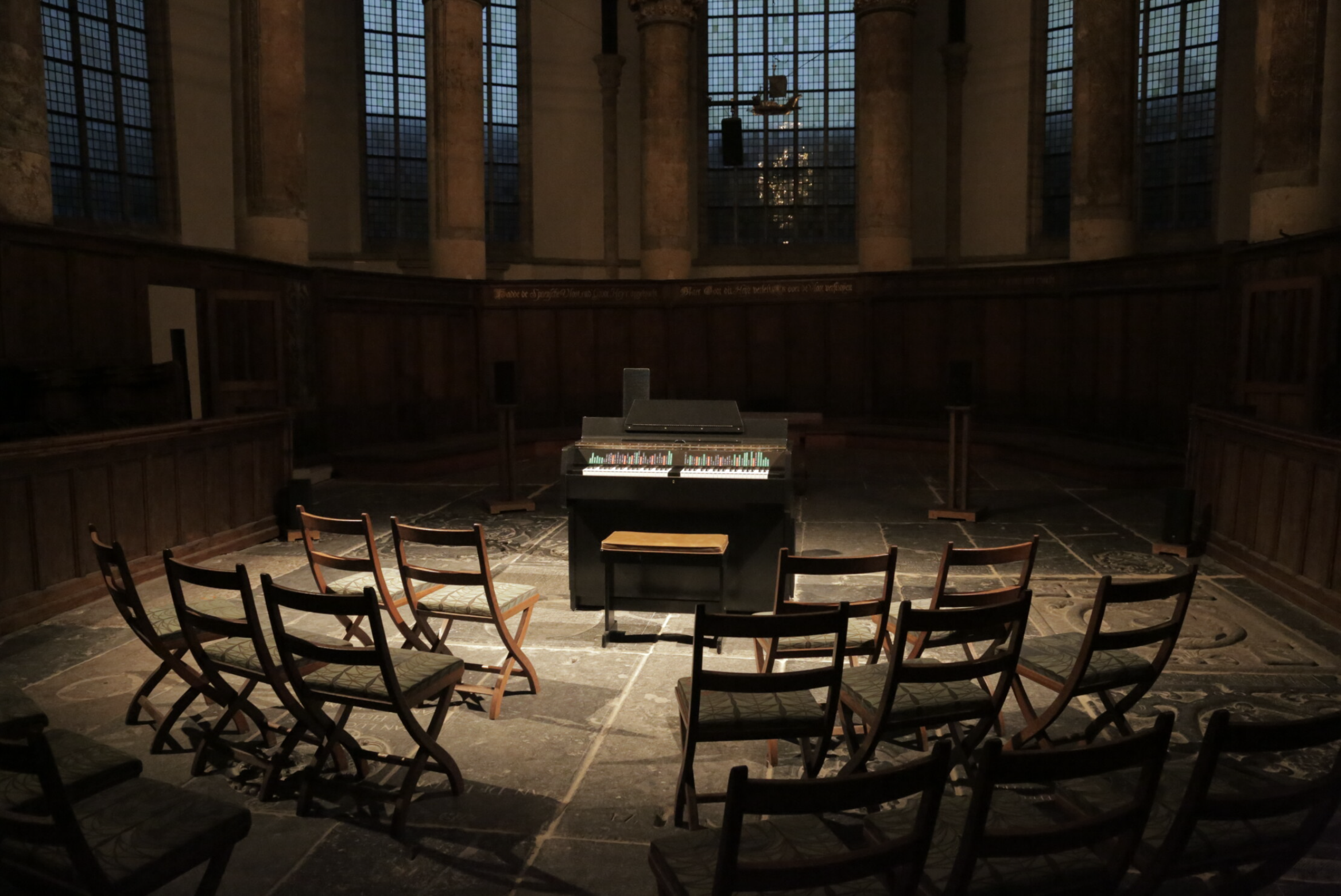 Color photograph of a piano and chairs facing the piano in the middle of an old church
