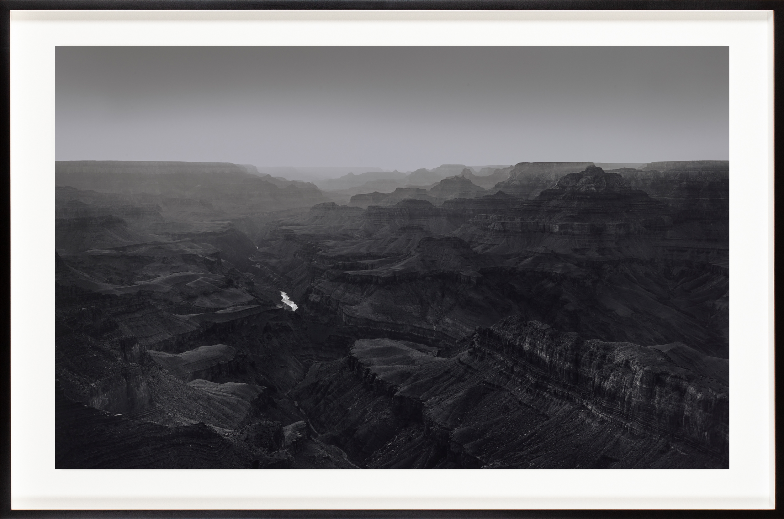 Black and white photograph of a desert canyon with a small river running through the center framed in black