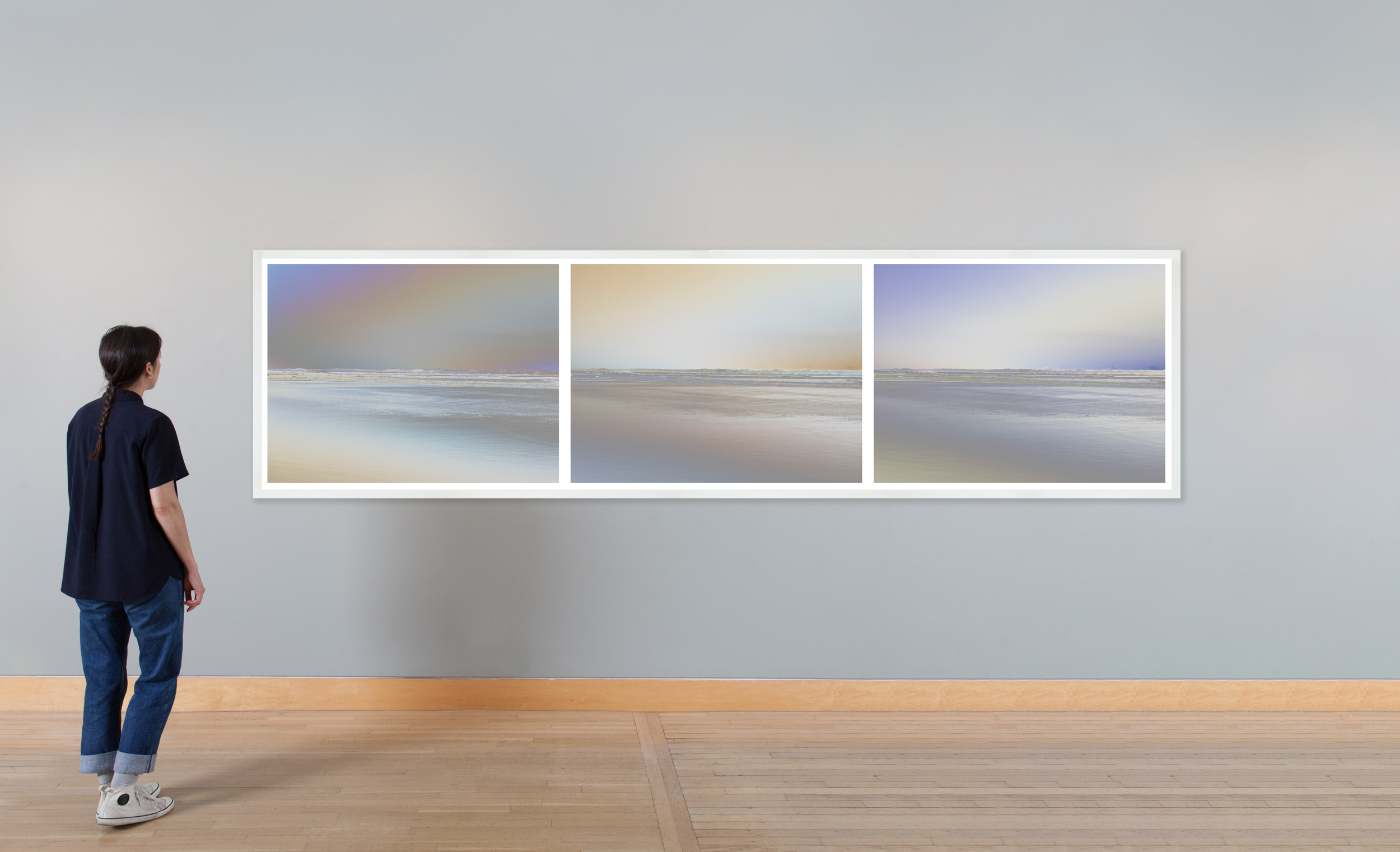 Color image of a figure looking at a triptych of color reversed photographs of the shoreline framed in white