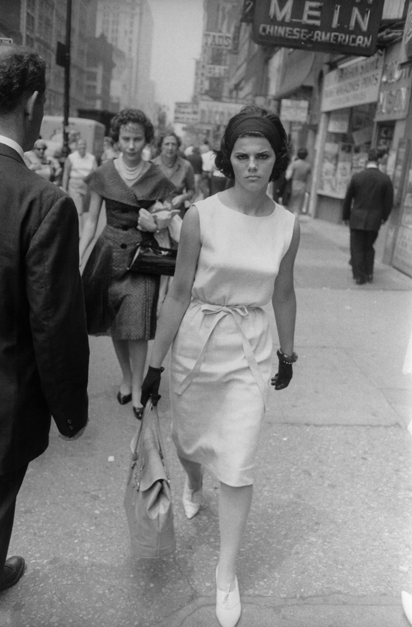 Black and white photograph of a female figure walking on a busy street