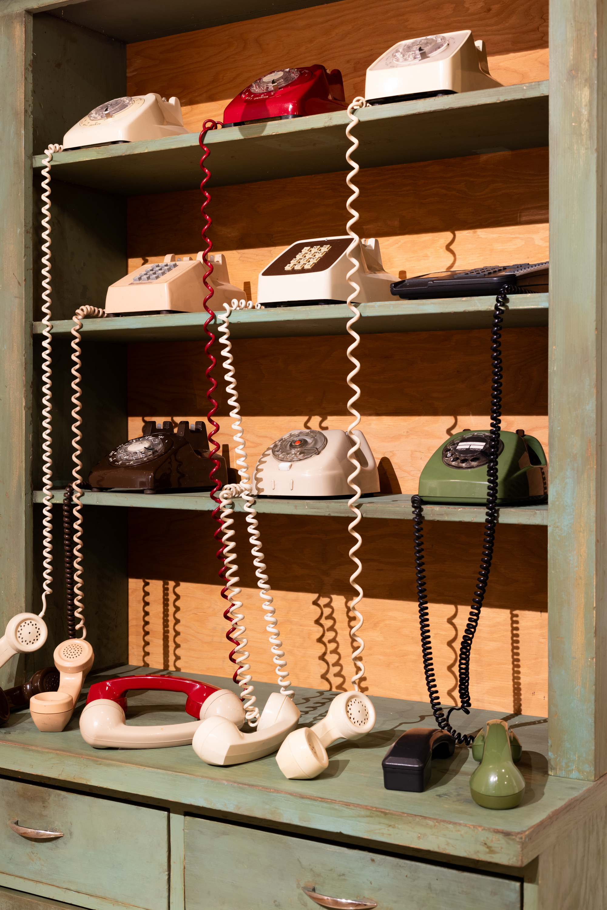 Color image of nine rotary phones on an aged green armoire