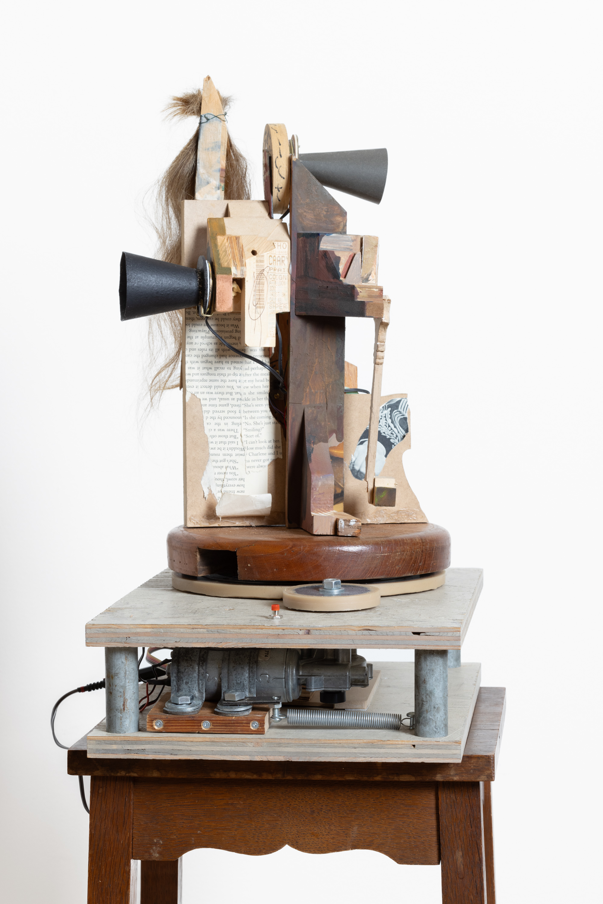 Color image of a mixed media artwork compromised of three gramophones and wooden pieces with collaged photographs and hair on a wooden pedestal