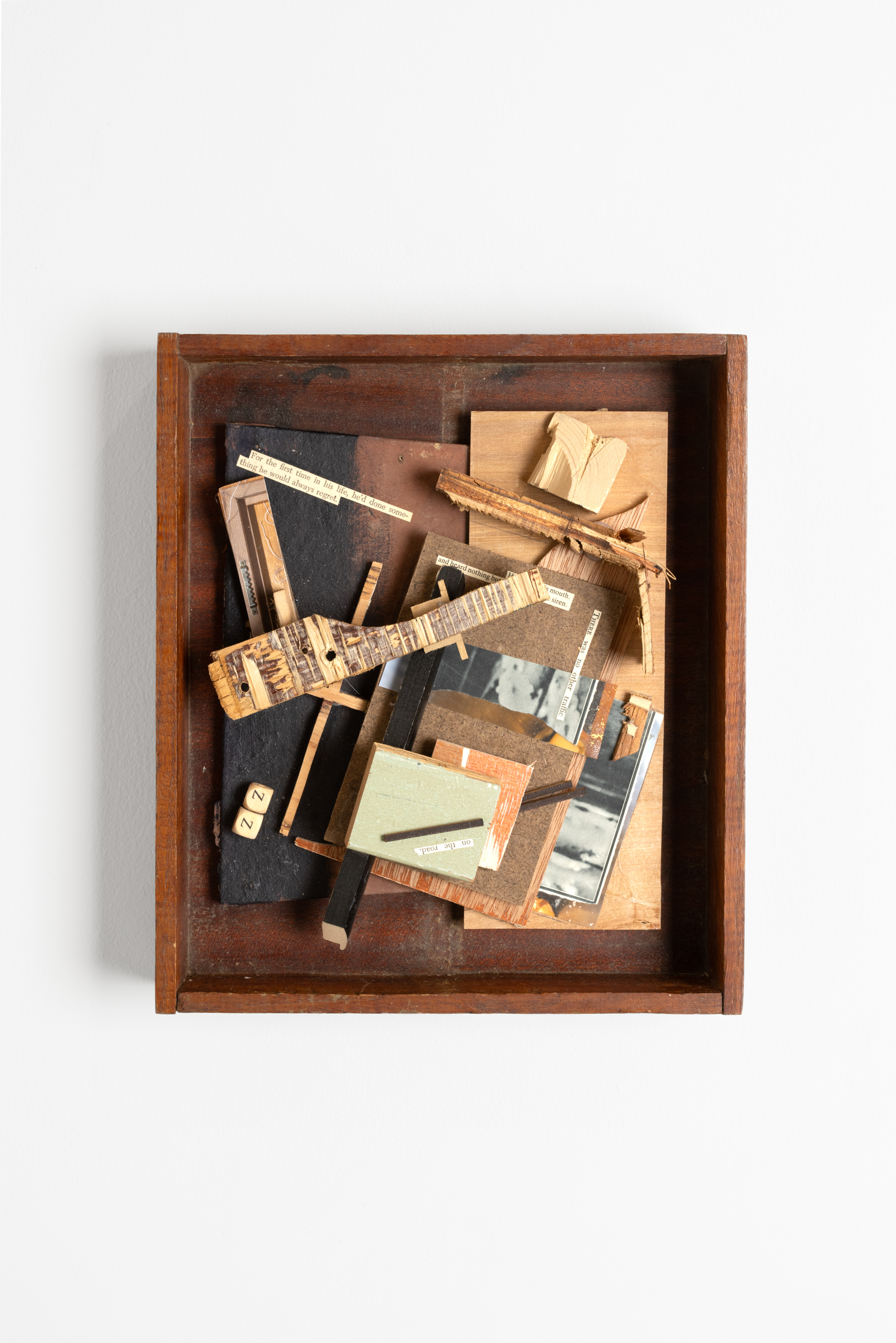Color image of a mixed media artwork with paper and photo collage on wooden pieces within a wooden box on a white wall