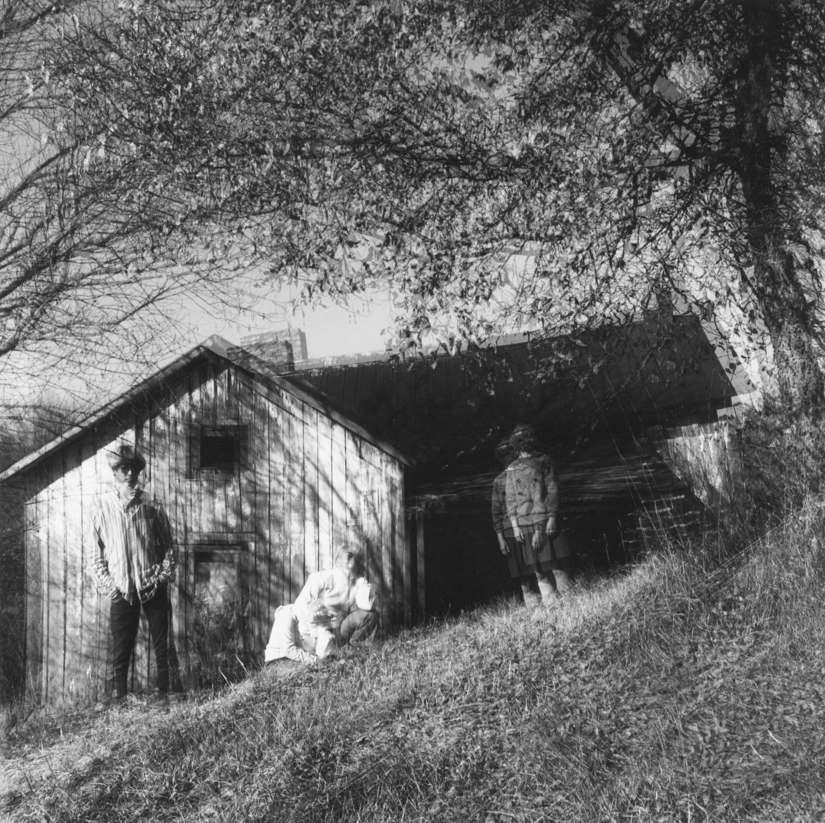Black and white photograph of three figures wearing masks standing outside an abandoned home with a blurred motion effect