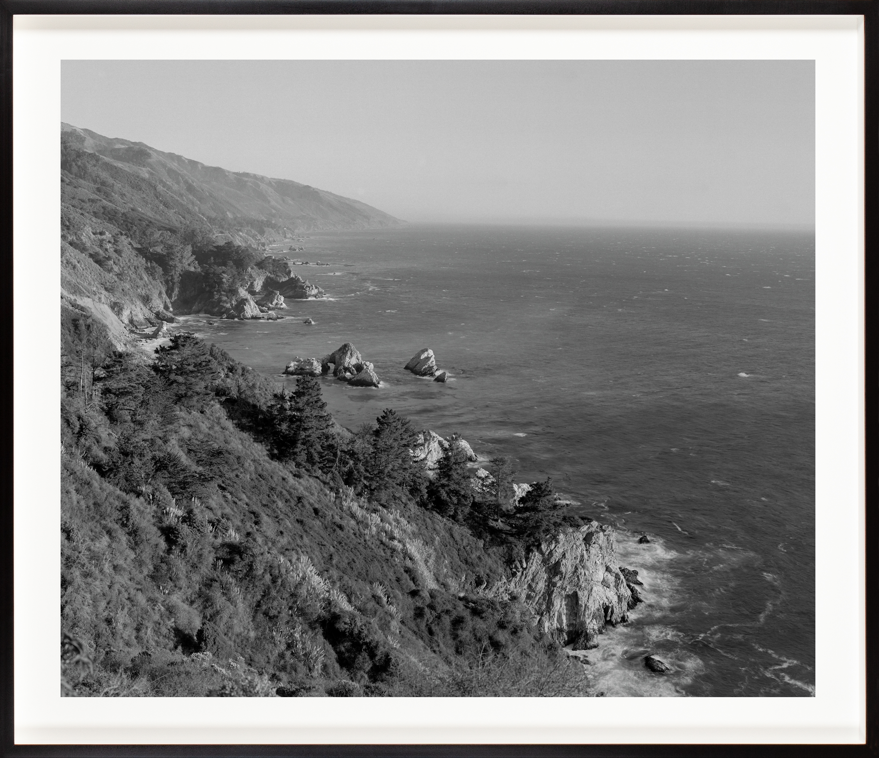 Black and white photograph of the coast meeting the ocean framed in black