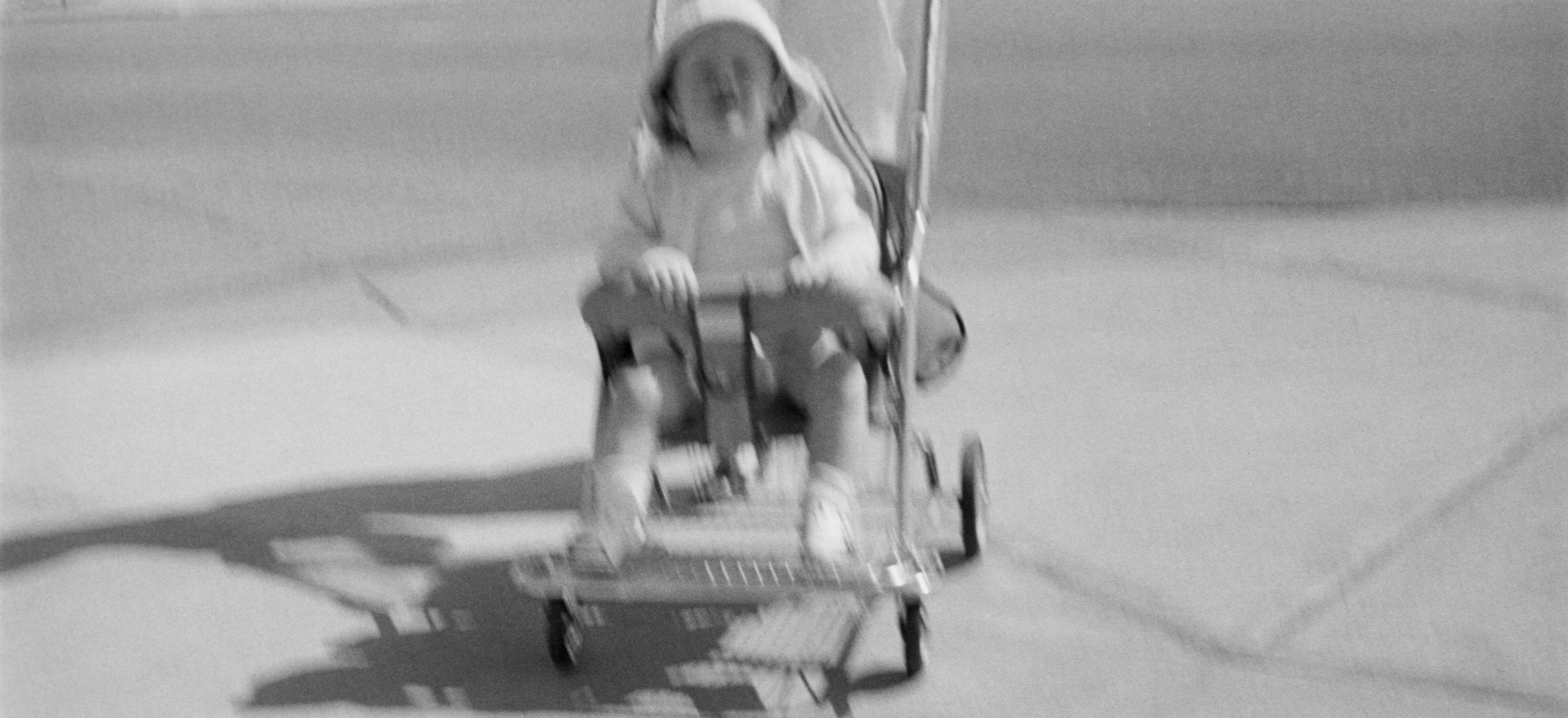 Black and white photograph of a child seated in a stroller on a sidewalk