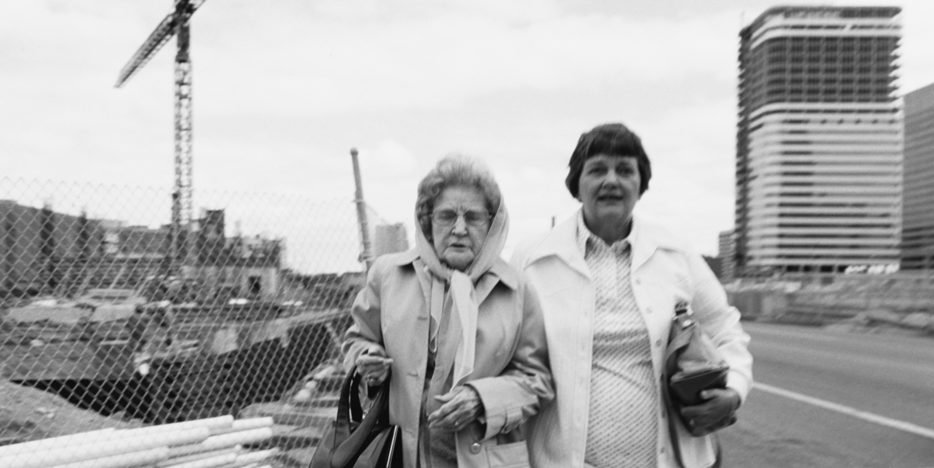 Black and white photograph of two female figures walking side by side outside amongst construction
