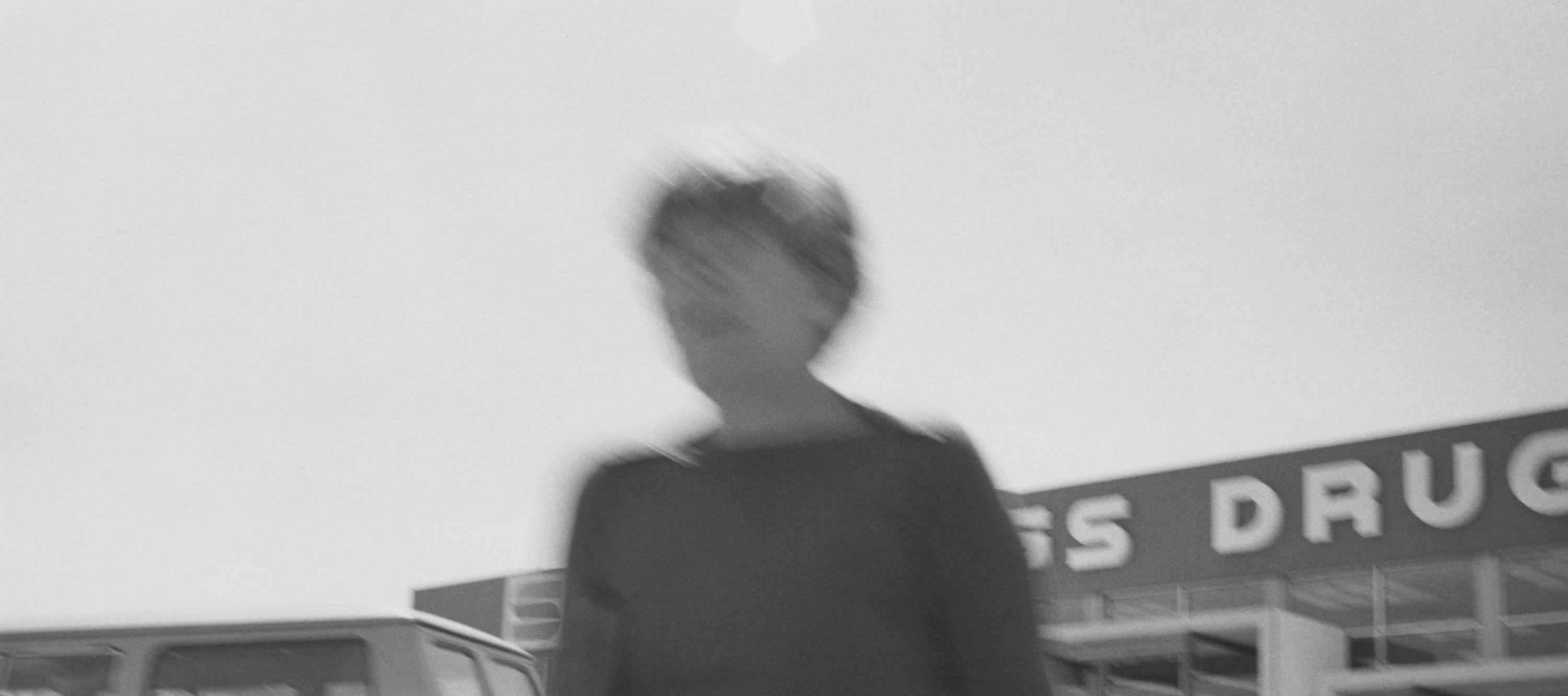 Black and white photograph of a figure blurred in front of a pharmacy