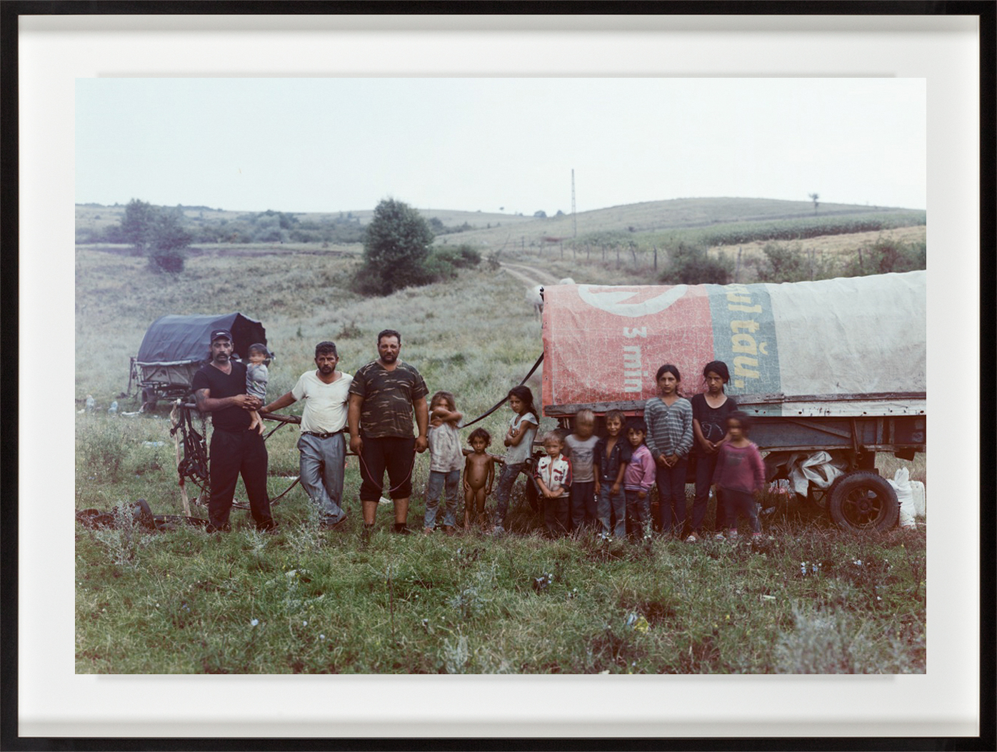 Color photograph of a large family standing besides a covered wagon outdoors framed in black