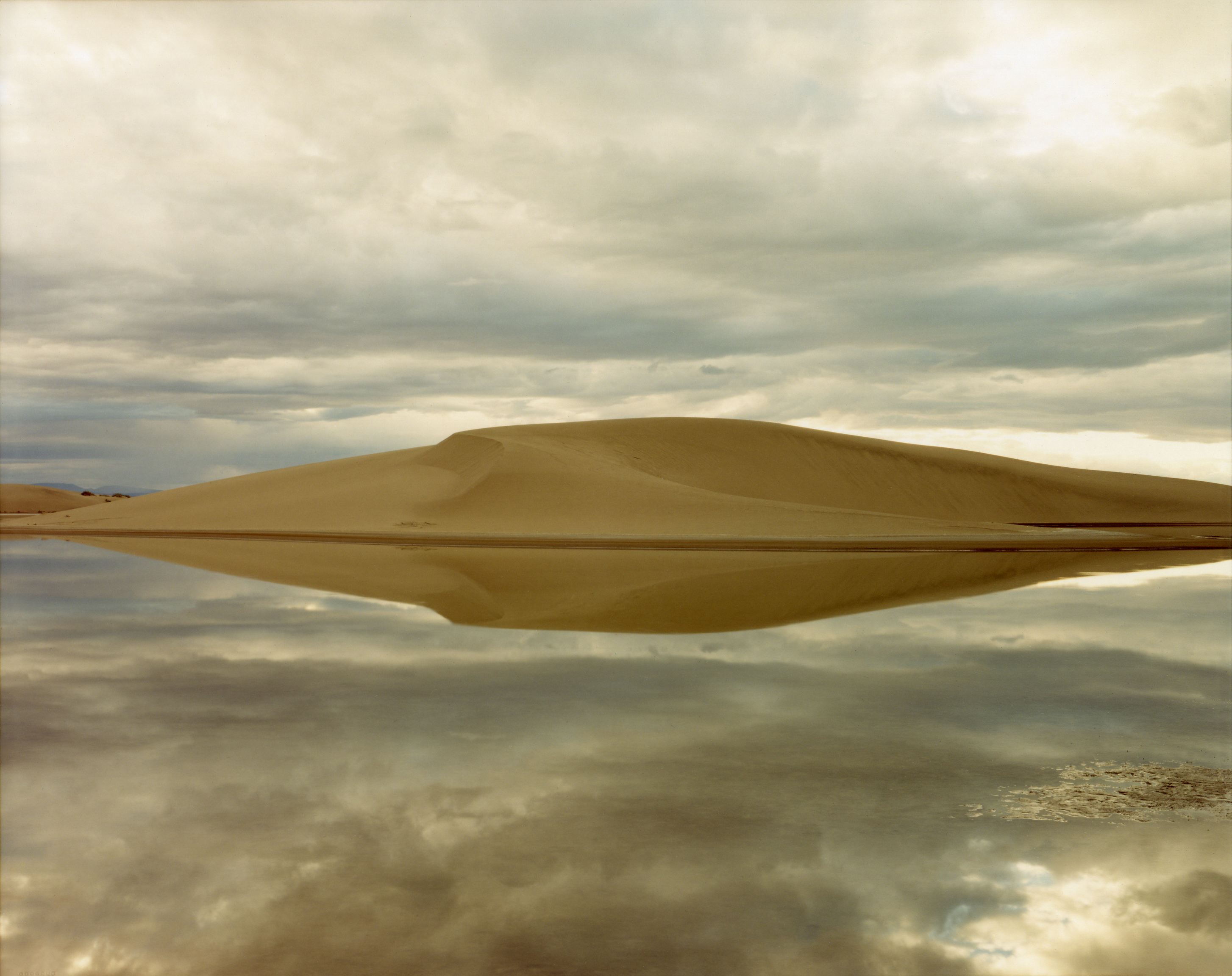 Color photograph of a large mound of sand in desert near body of water