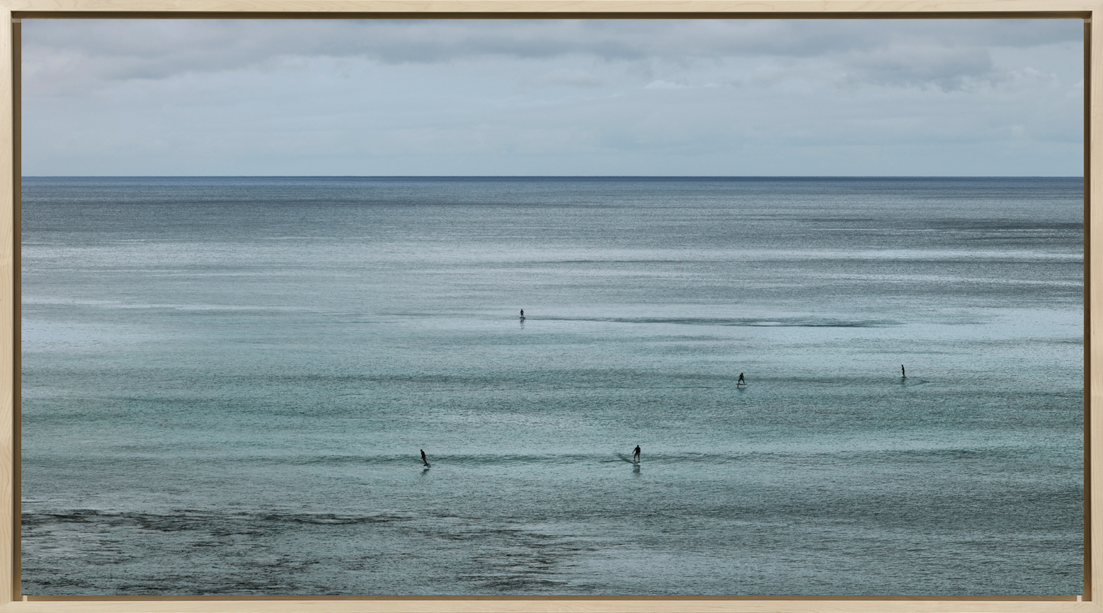 Color photograph of several wind surfers on the water framed in bleached wood