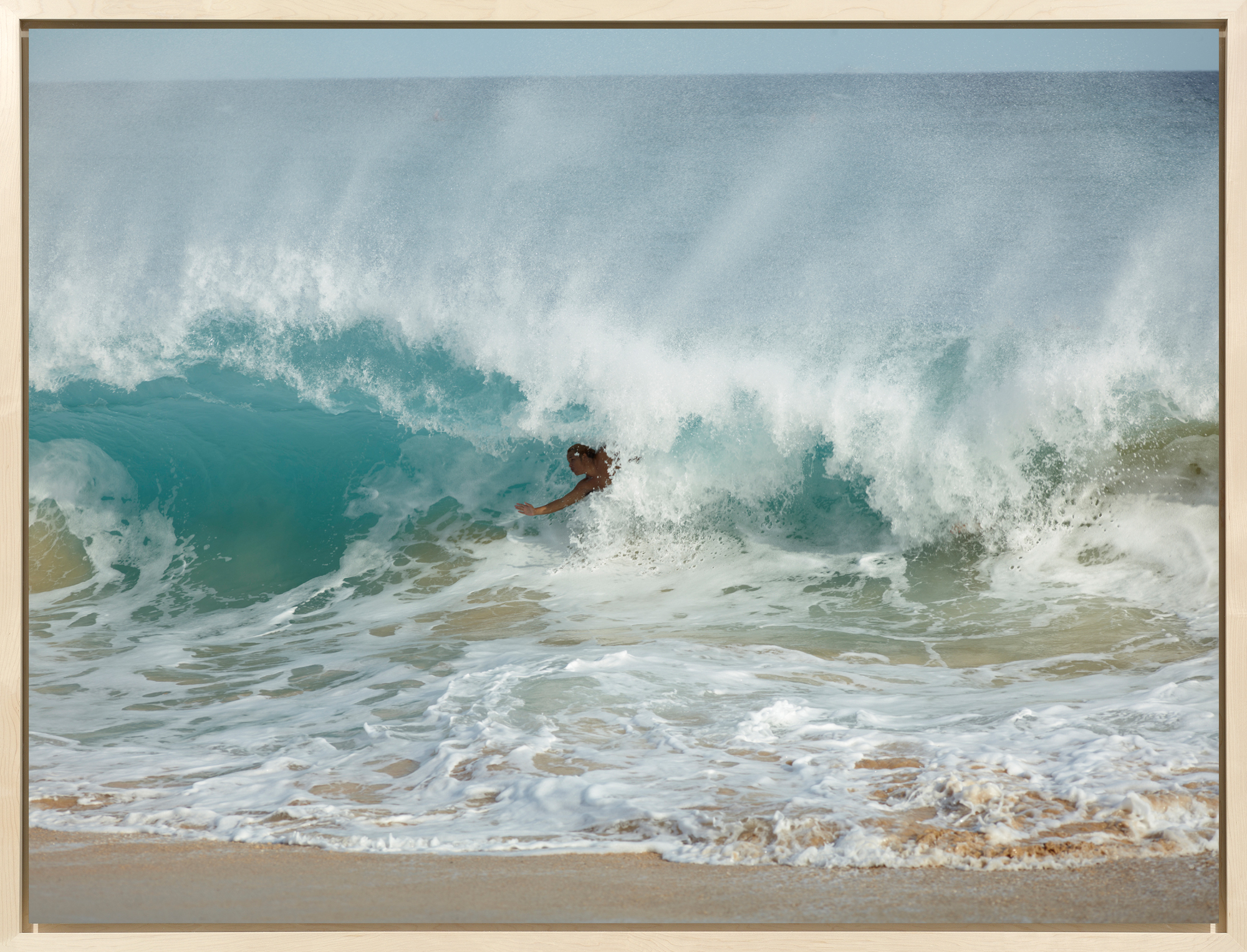 Color photograph of a surfer riding a wave as it crashes onto the shore framed in a bleached wood
