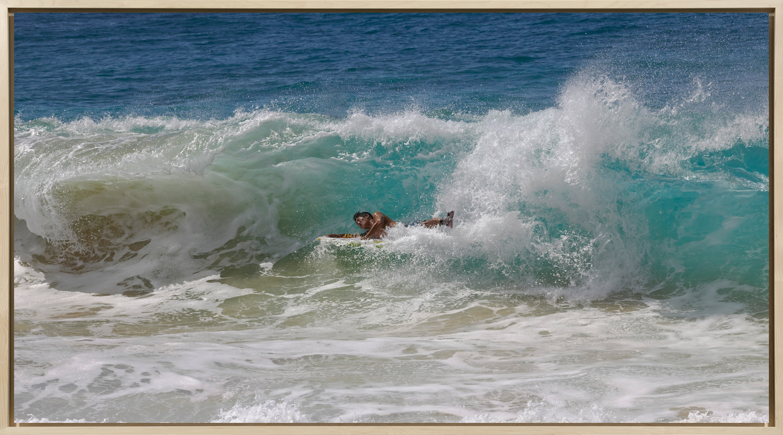 Color photograph of a surfer falling onto a wave of water framed in a bleached wood