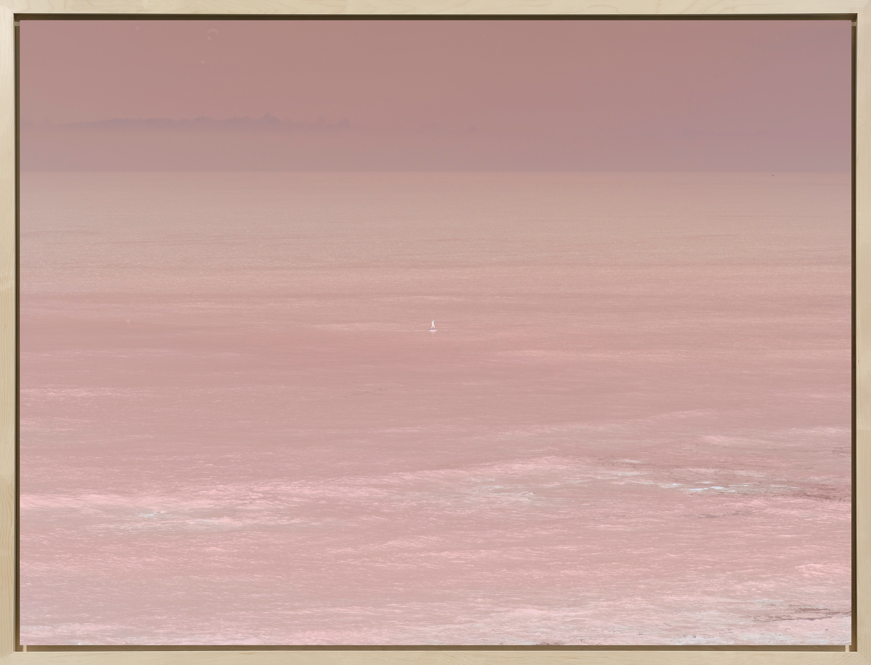 Color reversal photograph of a figure on a hydrofoil surfboard in the middle of calm pink waters framed in bleached wood