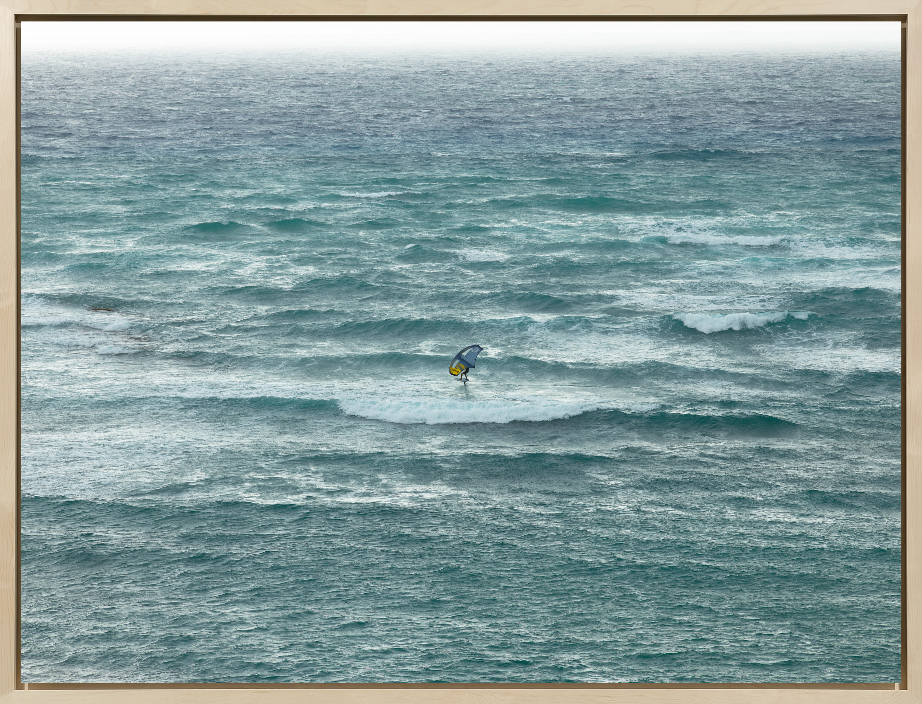 Color photograph of a windsurfer riding a wave in the middle of the ocean framed in bleached wood