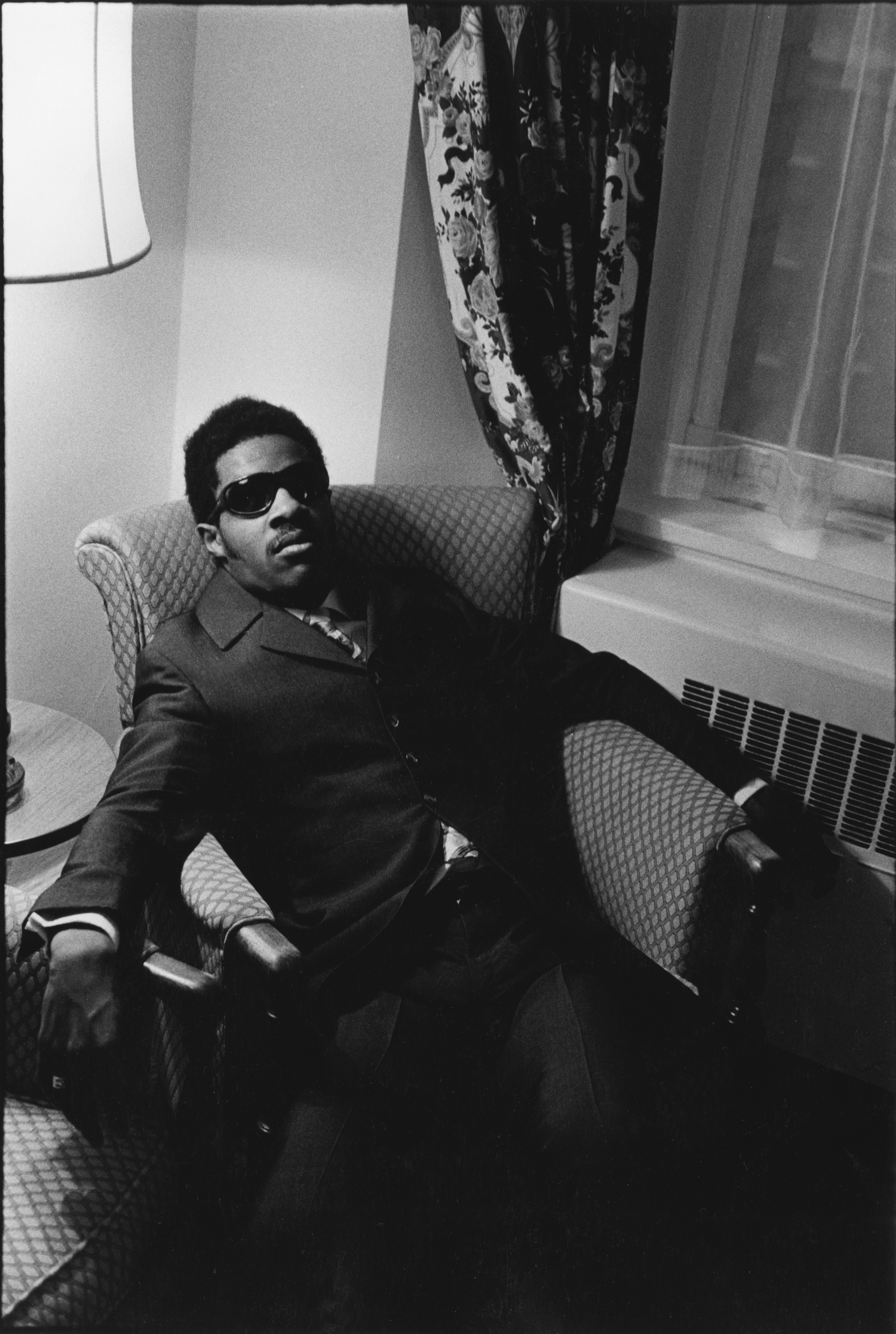 Black and white photograph of seated male figure in sunglasses and suit